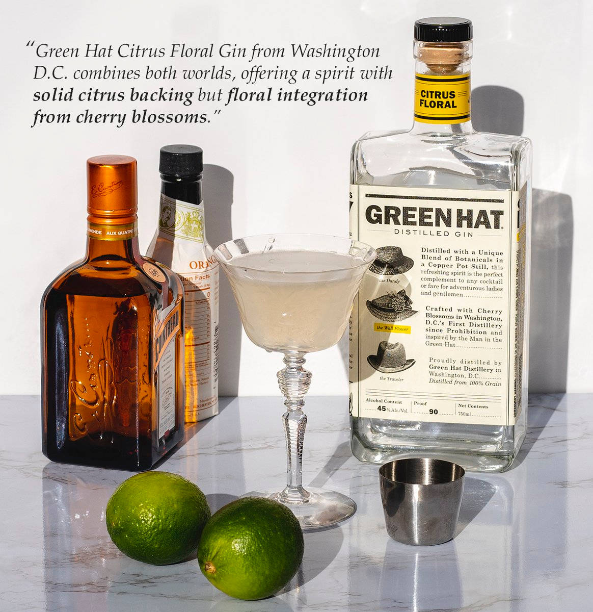 Gin 桌布 壁紙 — 一個時尚的靜物構圖，包含Green Hat Citrus Floral Gin酒瓶、雞尾酒杯和萊姆，置於大理石表面上，並有粗體文字疊加。