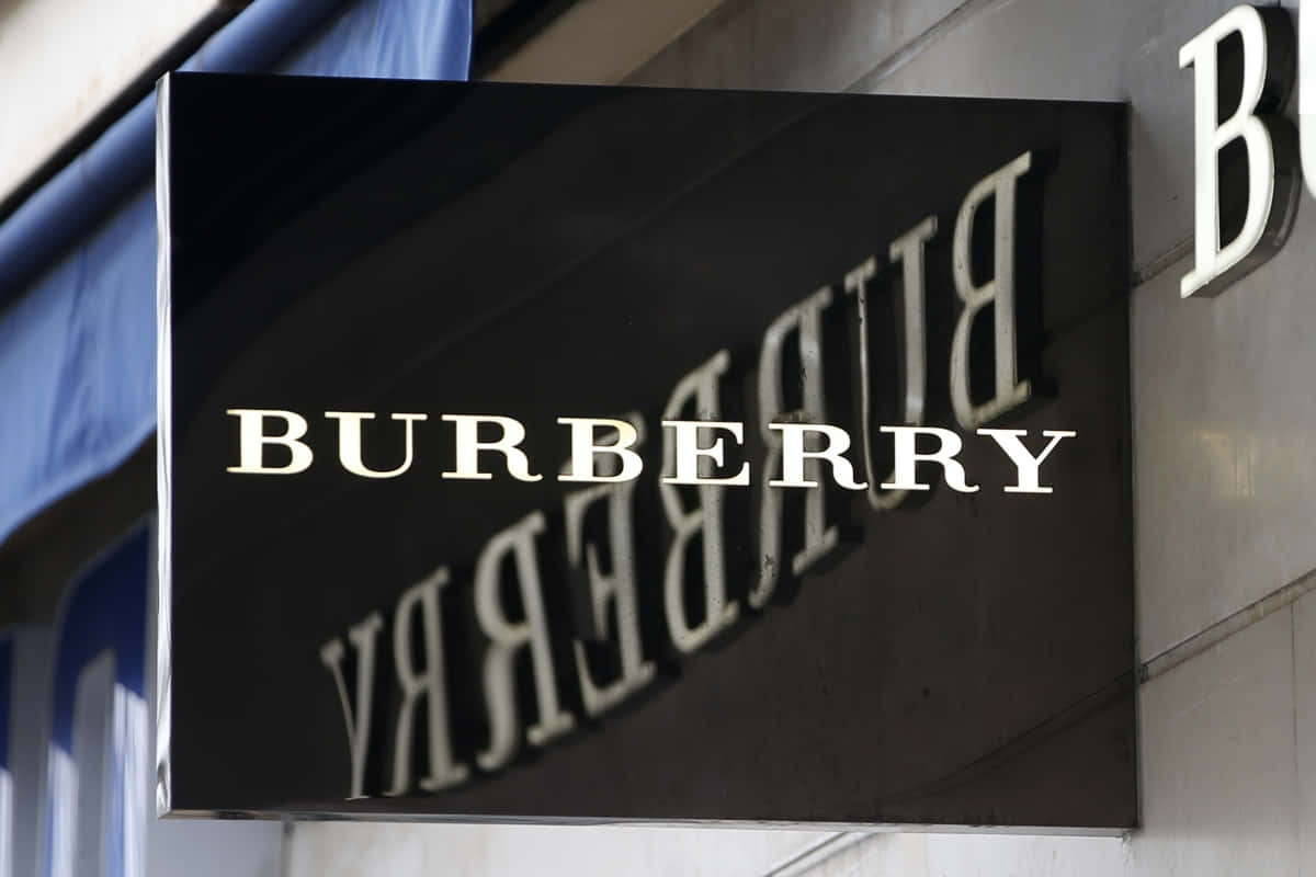 Burberry 桌布 壁紙 — 一個時尚的黑色 Burberry 標誌，帶有白色字體，安裝在建築物外牆上，在日光下。