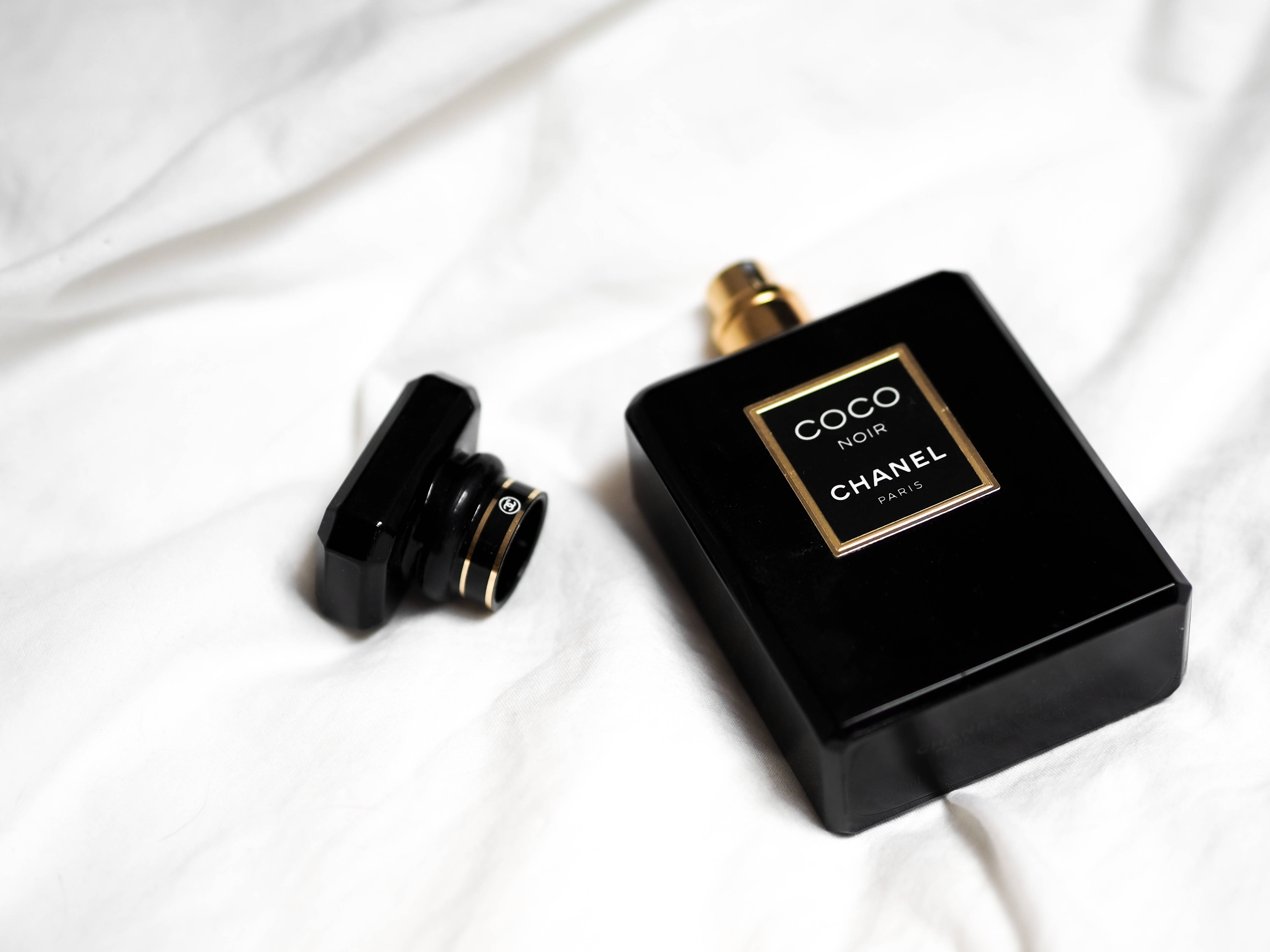 黑色美學 桌布 壁紙 — 一個時尚的黑色 Chanel Coco Noir 香水瓶，帶有金色點綴，放置在柔軟的白色布料背景上。