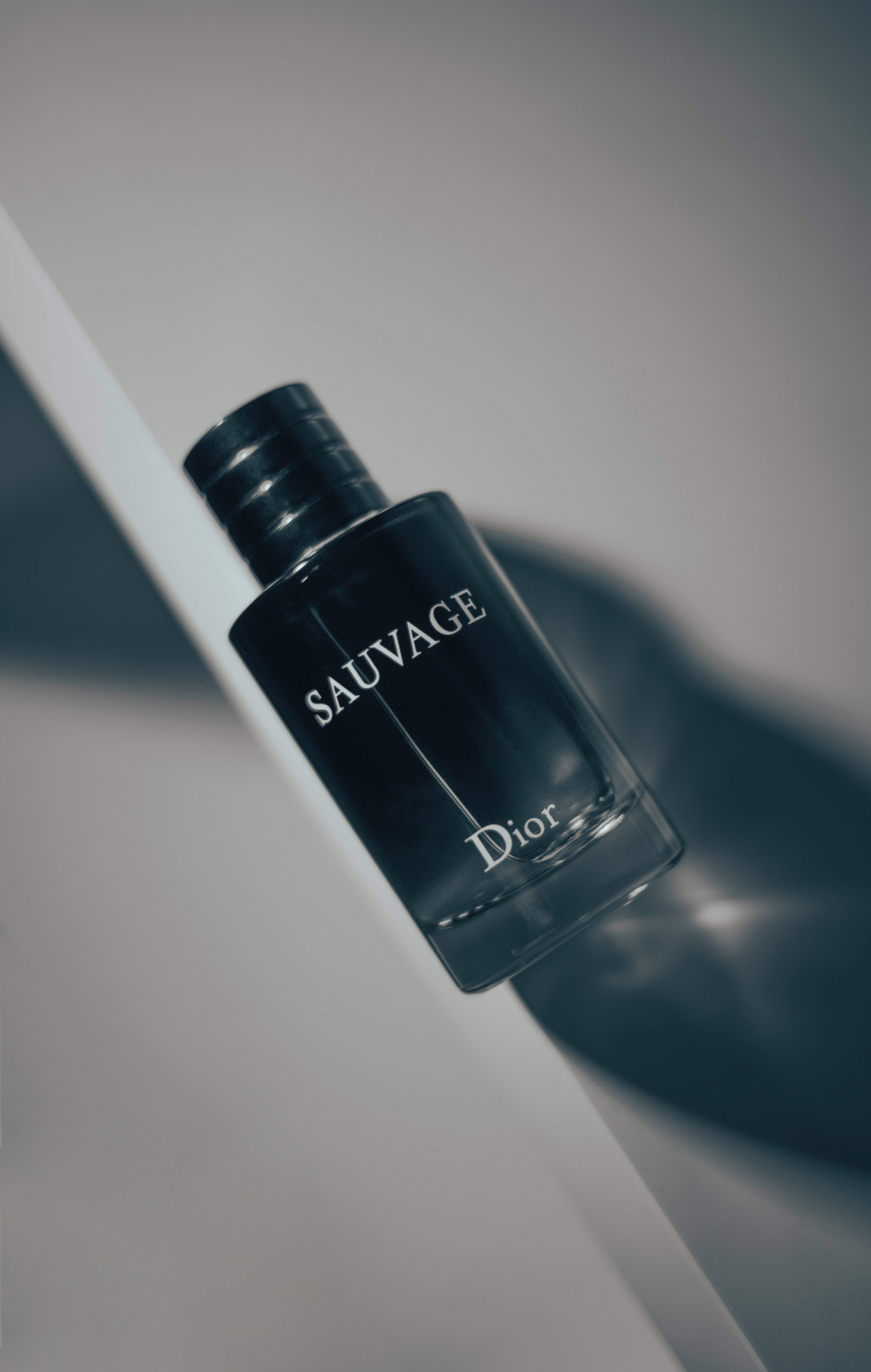 桌布 壁紙 — 一個時尚的黑色 Dior Sauvage 香水瓶放置在白色表面上，帶有柔和陰影和極簡燈光。