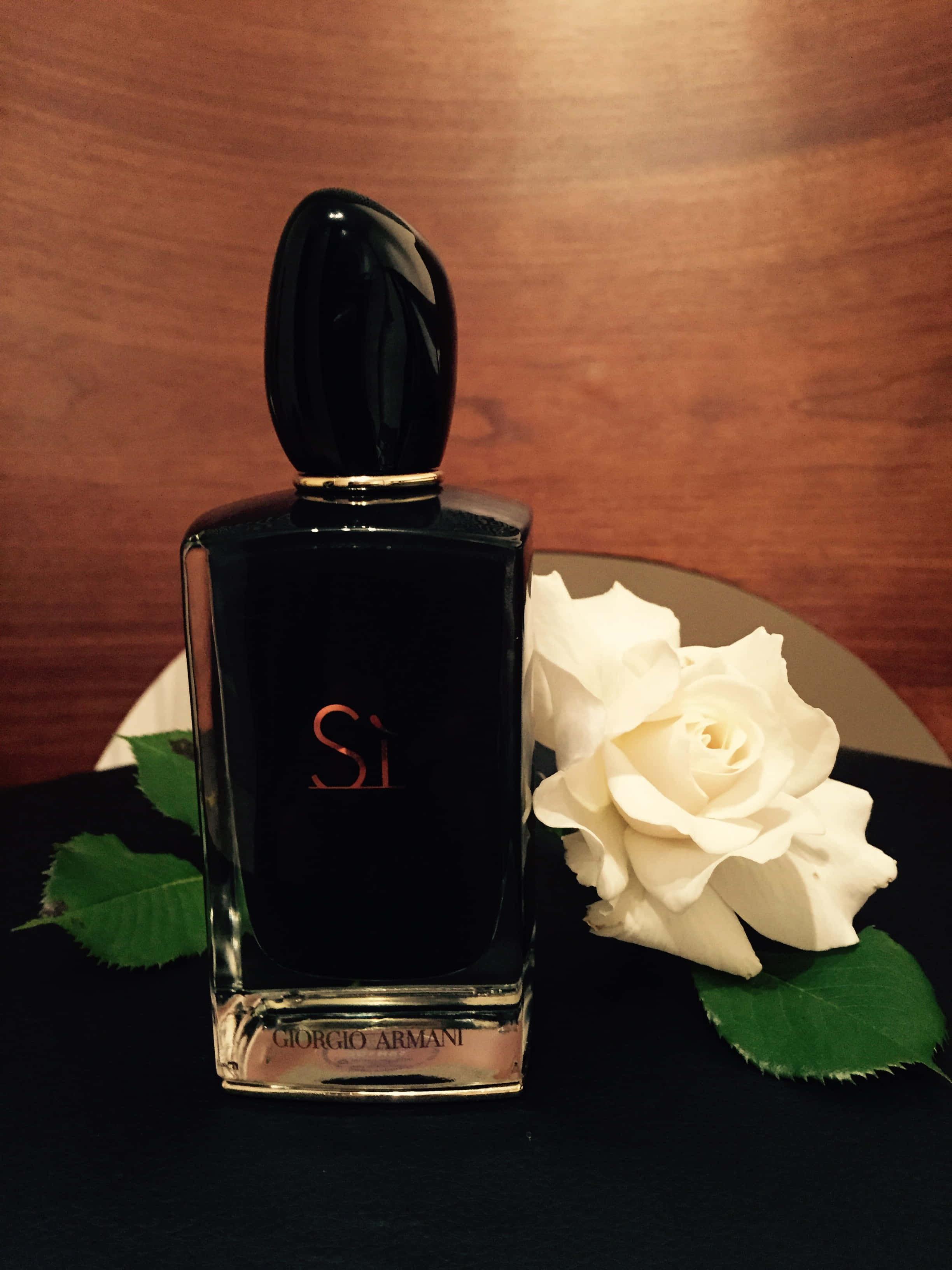 perfume 桌布 壁紙 — 一個時尚的黑色 Giorgio Armani Si 香水瓶放在一個溫暖的木質背景下的深色表面上，旁邊是一朵純潔的白玫瑰。