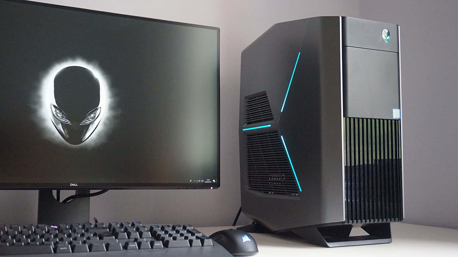 外星人 桌布 壁紙 — 一個時尚的黑色Alienware桌面塔，帶有發光的藍色點綴，旁邊是一個顯示標誌性外星人頭標誌的顯示器。