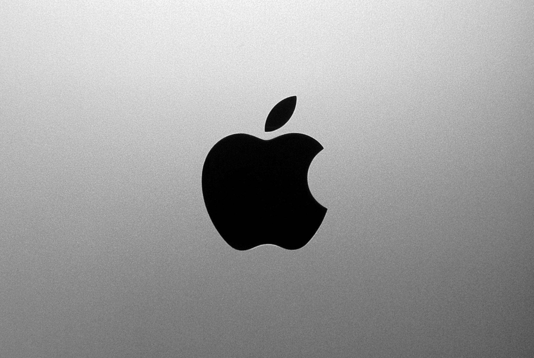 4K 桌布 壁紙 — 一個時尚的黑色Apple標誌，位於拉絲銀色筆記型電腦蓋中央，帶有柔和漸變照明。