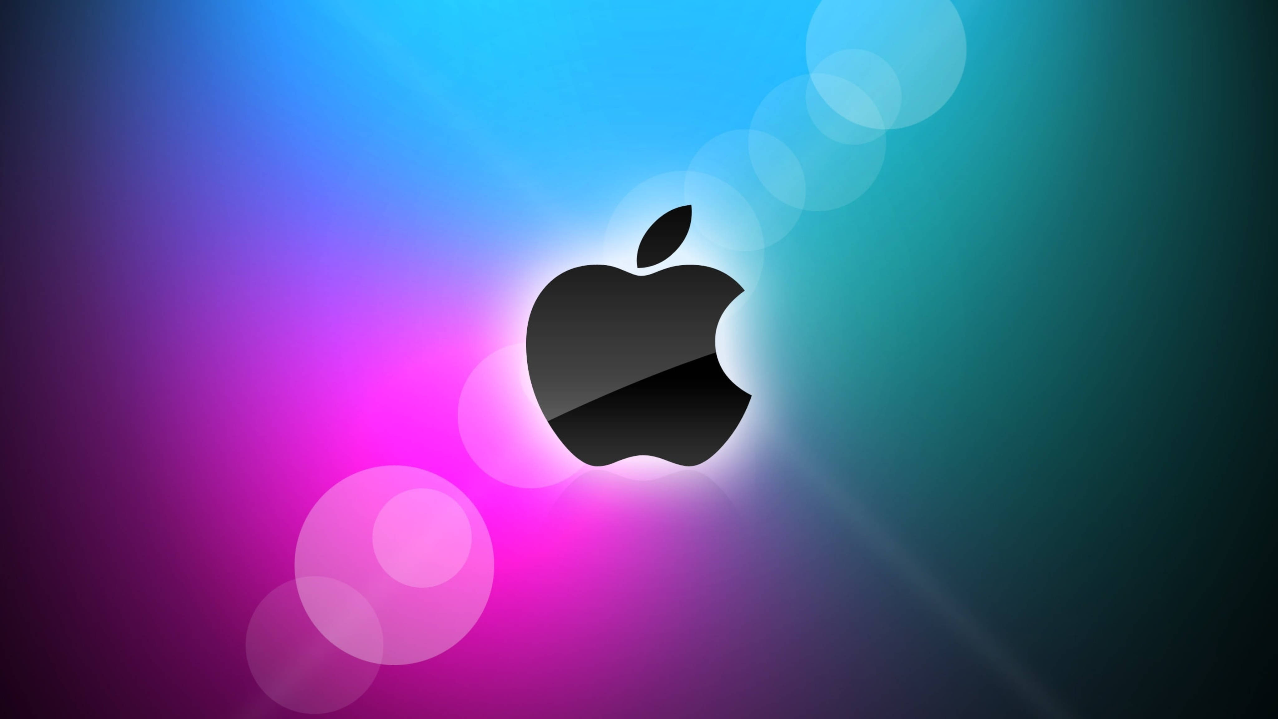 Apple 4K Ultra HD 桌布 壁紙 — 一個時尚的黑色Apple標誌在藍色、紫色和藍綠色的鮮豔漸變背景上發光，並帶有柔和的散景燈光。