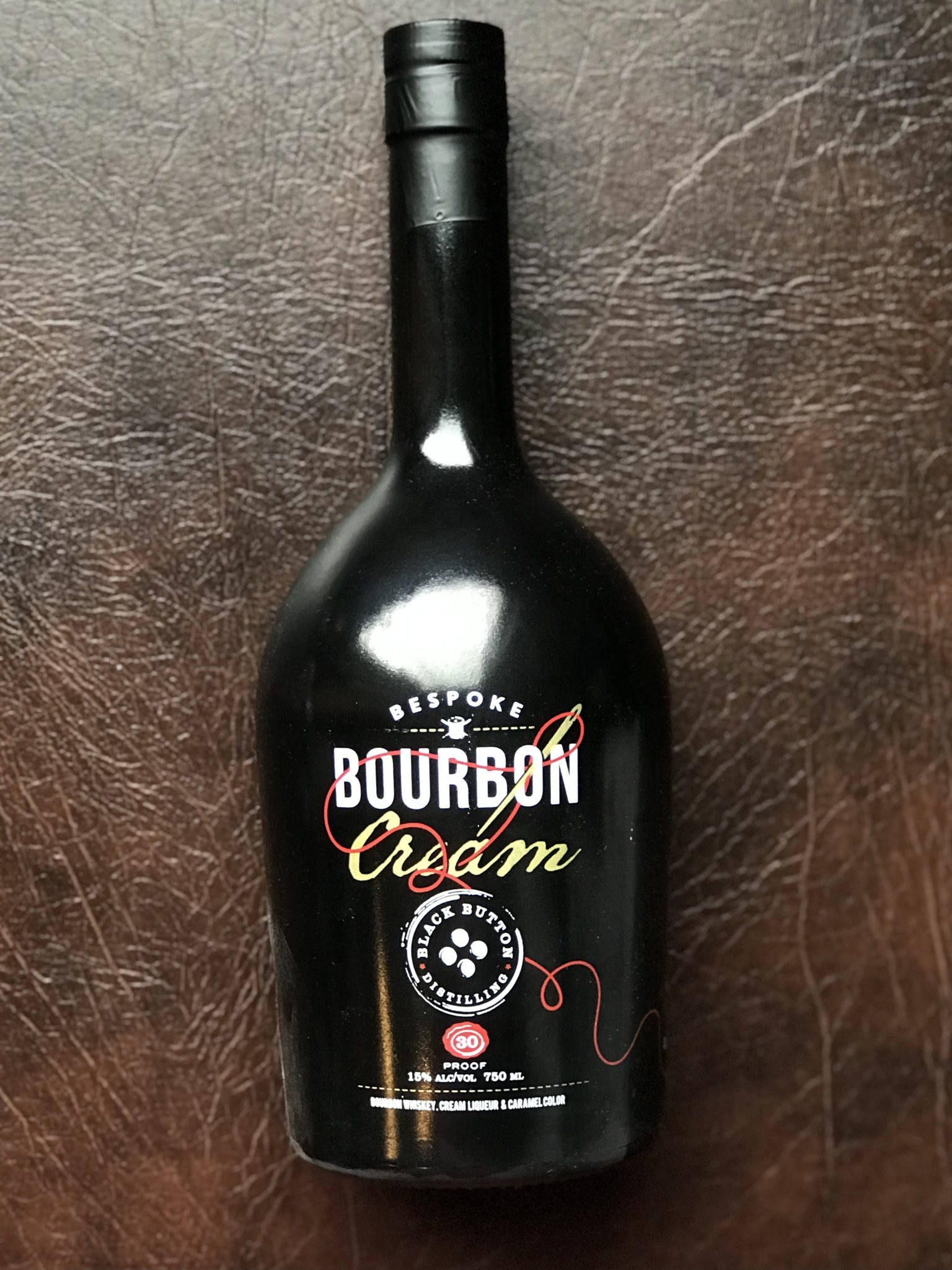 奶油色 桌布 壁紙 — 一個時尚的黑色Bespoke Bourbon Cream利口酒瓶放置在質感豐富的棕色皮革表面上。