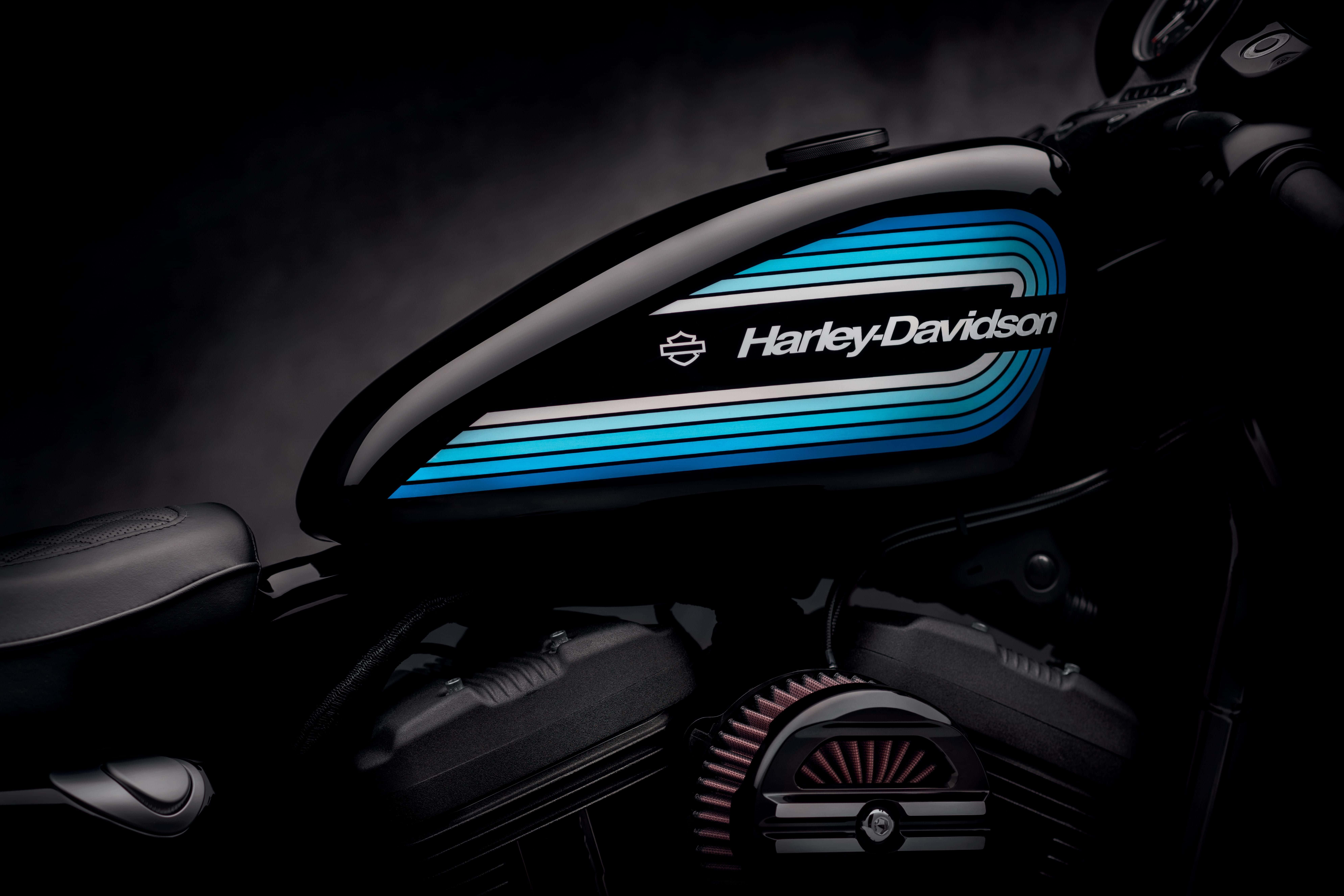 Gambar 桌布 壁紙 — 一個時尚的黑色Harley-Davidson摩托車油箱，帶有醒目的藍色和白色條紋，在戲劇性的工作室燈光下閃耀。
