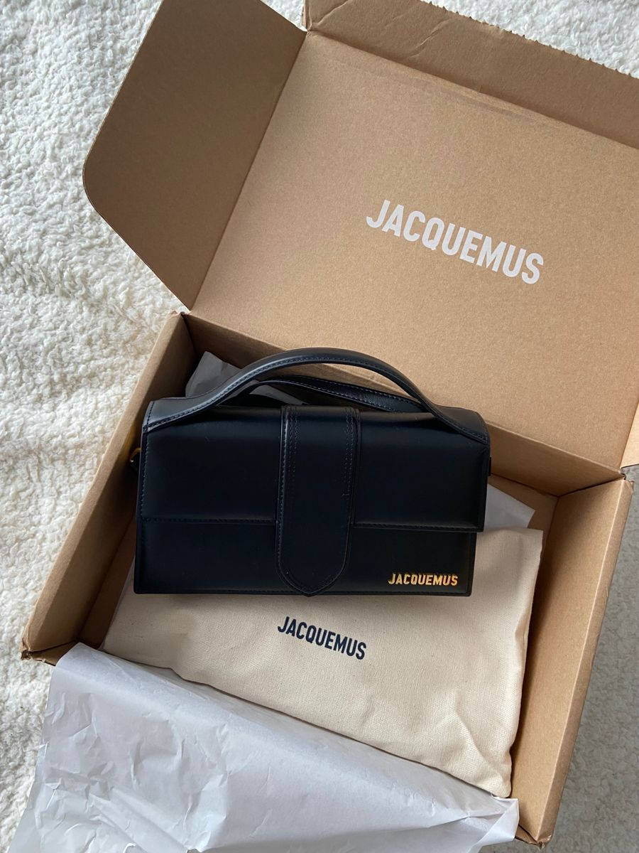 Handbag 桌布 壁紙 — 一個時尚的黑色Jacquemus手提包放在其品牌盒子內，置於柔軟的白色地毯上。