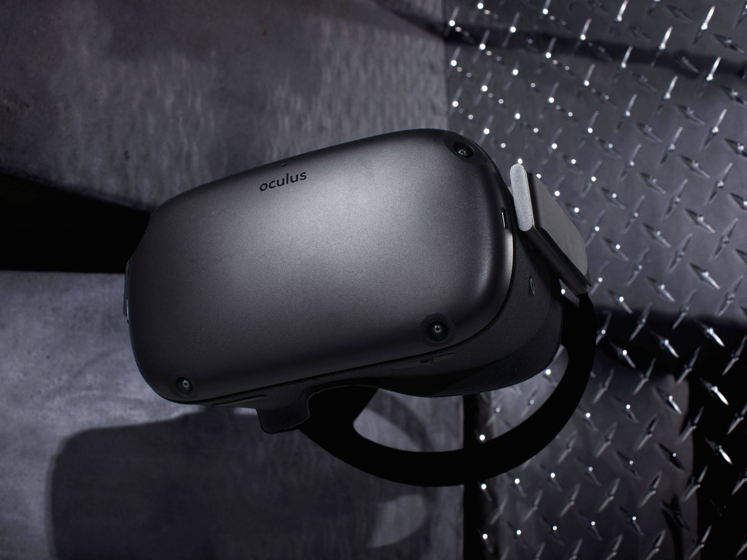Quest 桌布 壁紙 — 一個時尚的黑色Oculus VR頭戴式裝置放置在紋理金屬表面上，在戲劇性的工作室燈光下。