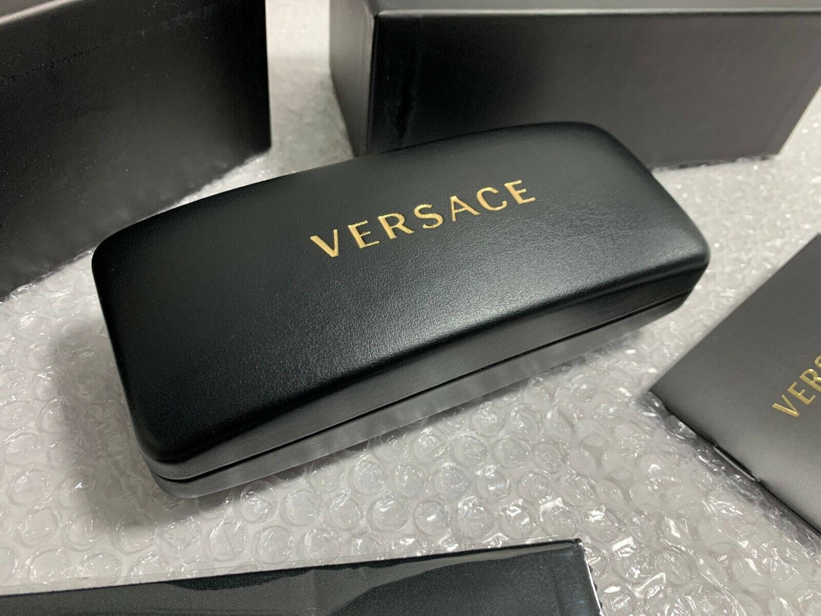 Sunglasses 桌布 壁紙 — 一個時尚的黑色Versace太陽眼鏡盒，帶有金色字樣，放在氣泡包裝上，旁邊是相配的盒子。