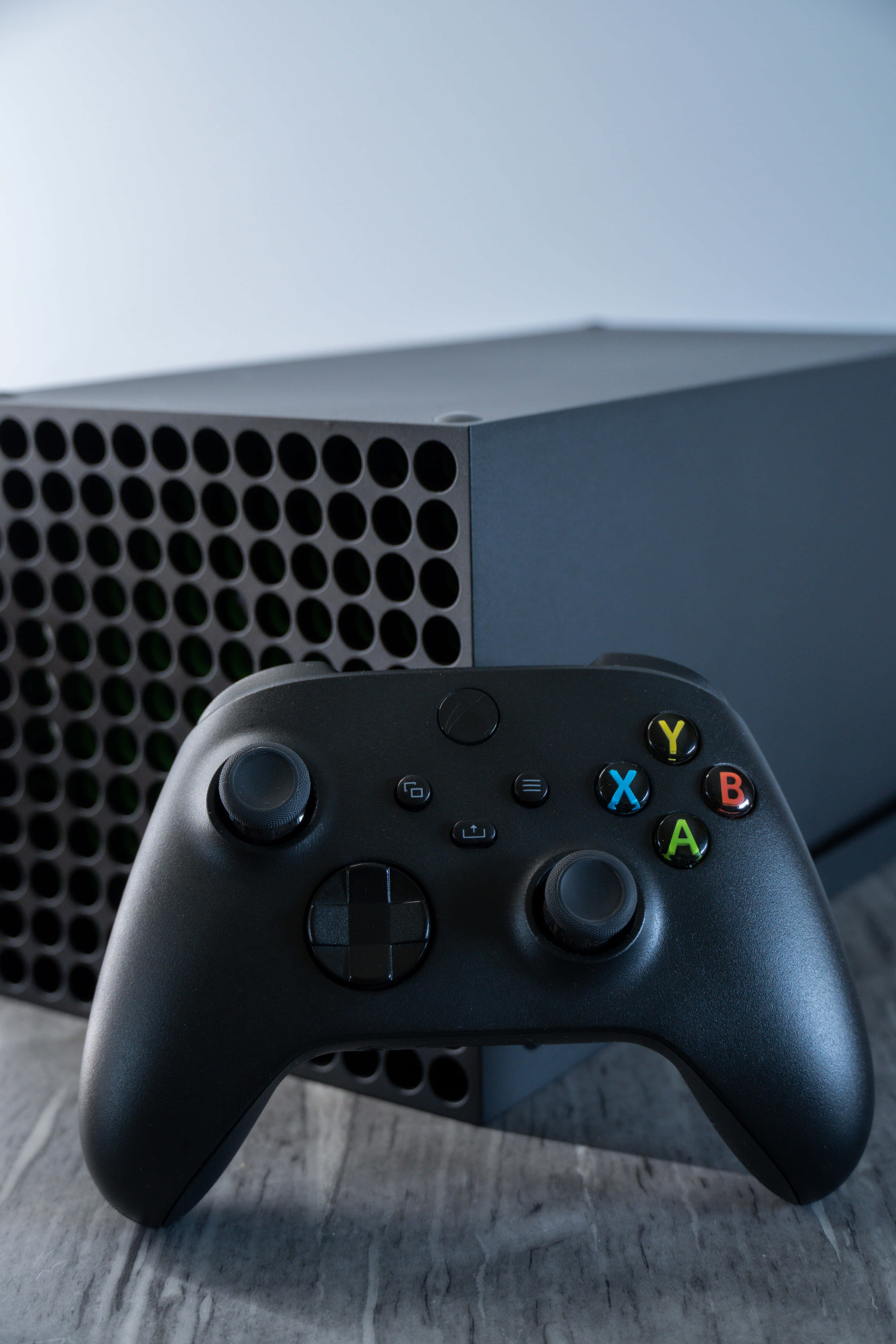 Gaming Consoles 桌布 壁紙 — 一個時尚的黑色Xbox手把放在一個相配的主機前面，置於有紋理的木質表面上。
