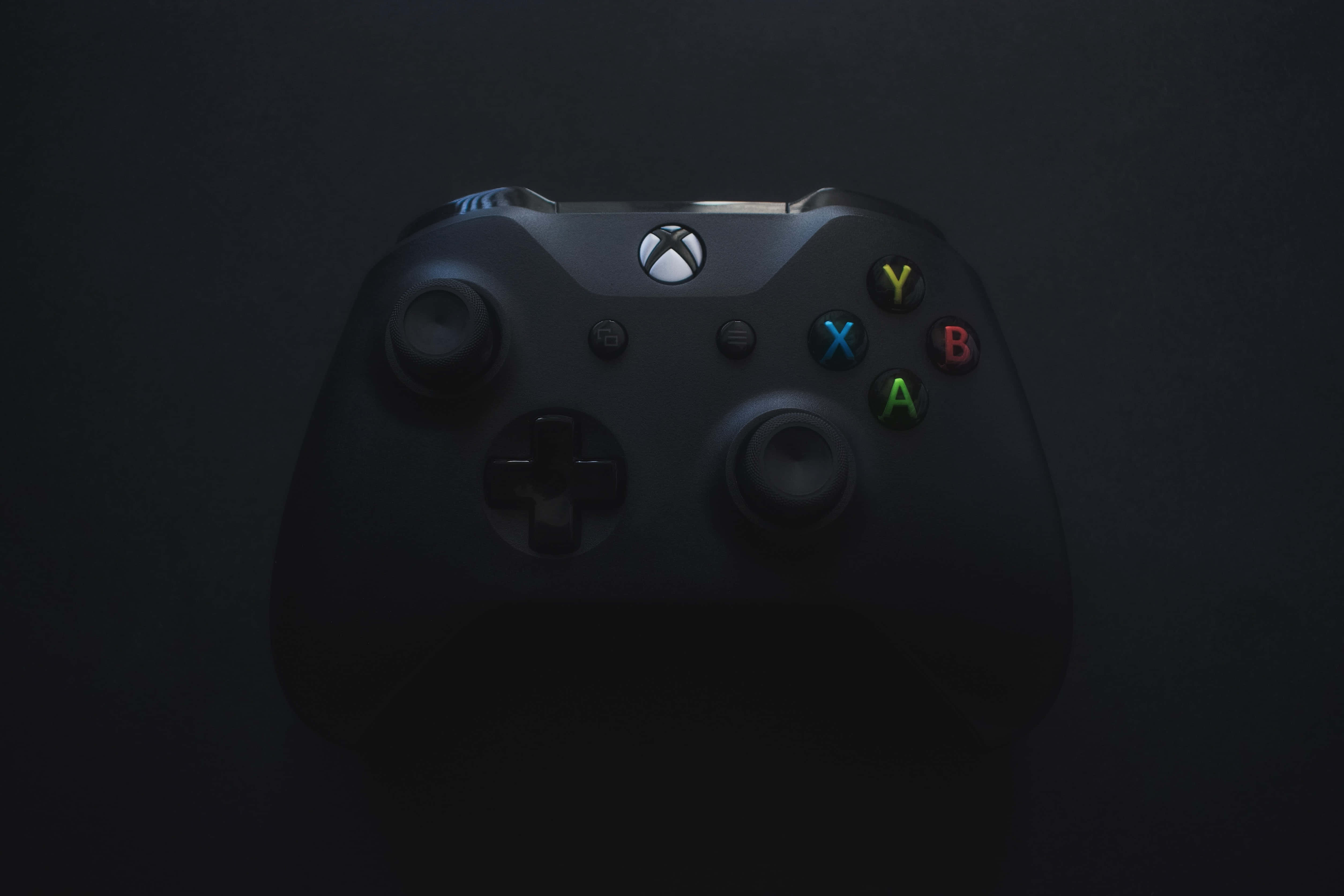 4K Gaming Consoles 桌布 壁紙 — 一個時尚的黑色Xbox控制器，在黑暗背景下被柔和光線照亮。