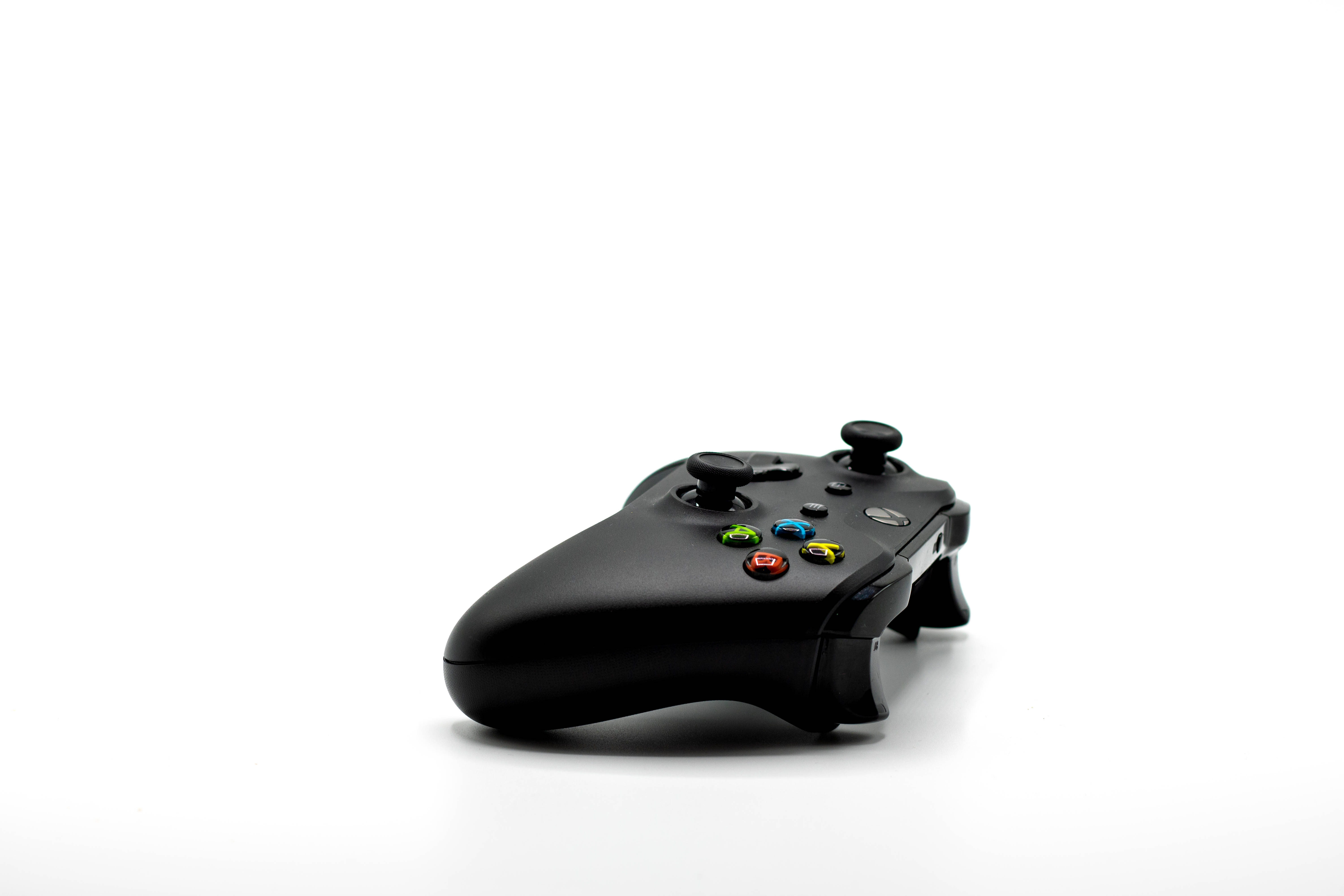 雷蛇 桌布 壁紙 — 一個時尚的黑色Xbox控制器，帶有彩色按鈕，放置在潔白的表面上。