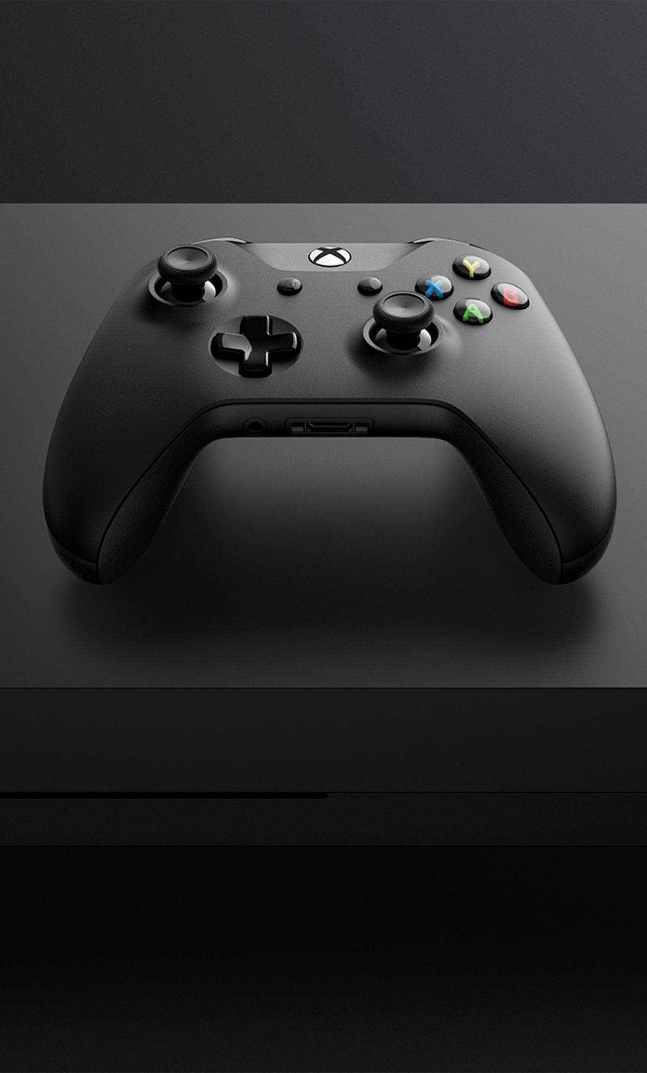 Xbox 桌布 壁紙 — 一個時尚的黑色Xbox控制器放在深色表面上，在柔和的攝影棚燈光下突顯其符合人體工學的設計和色彩繽紛的按鈕。