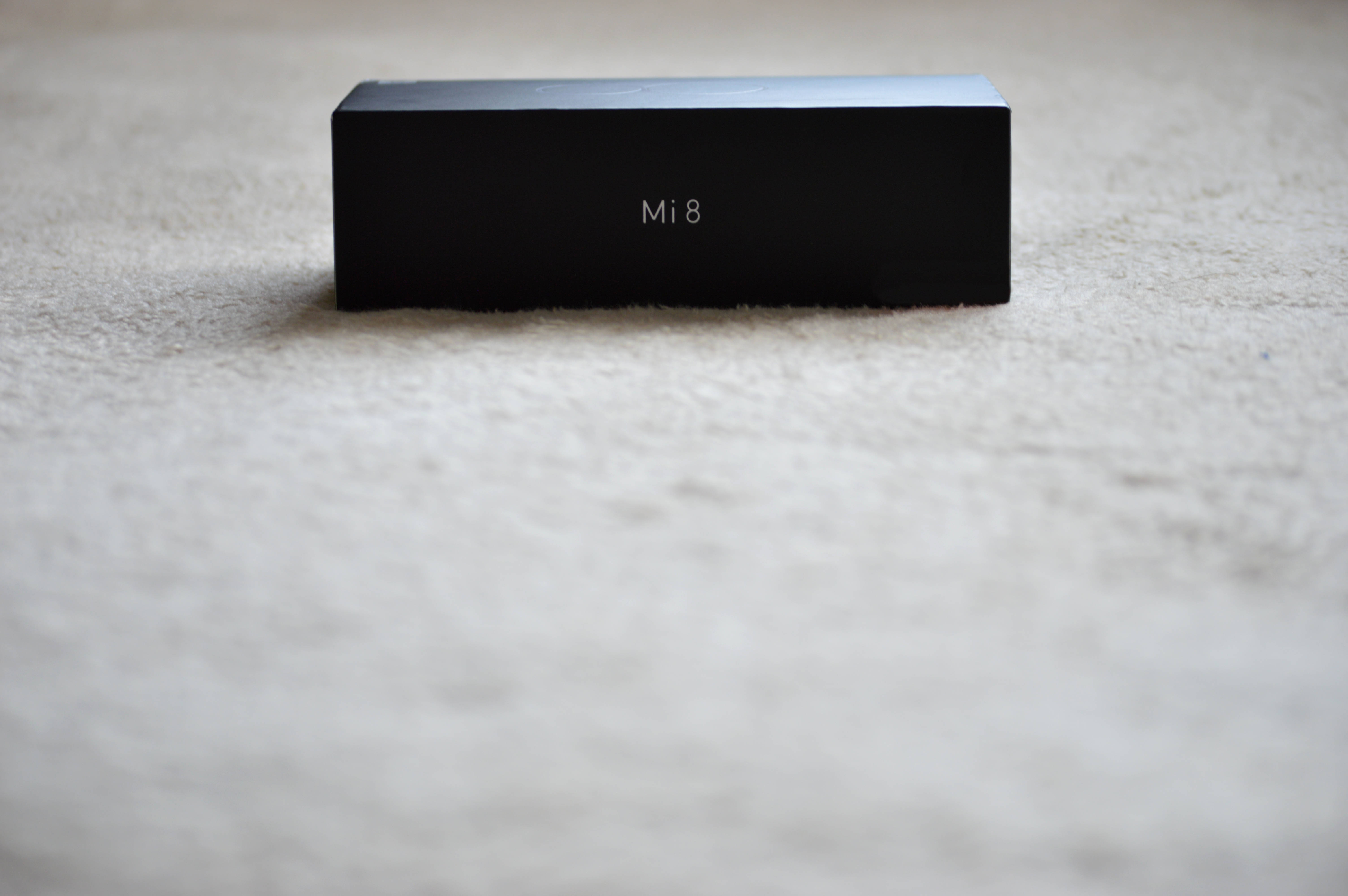 Xiaomi 桌布 壁紙 — 一個時尚的黑色Xiaomi Mi 8盒子居中放置在柔軟的米色地毯上，景深較淺。