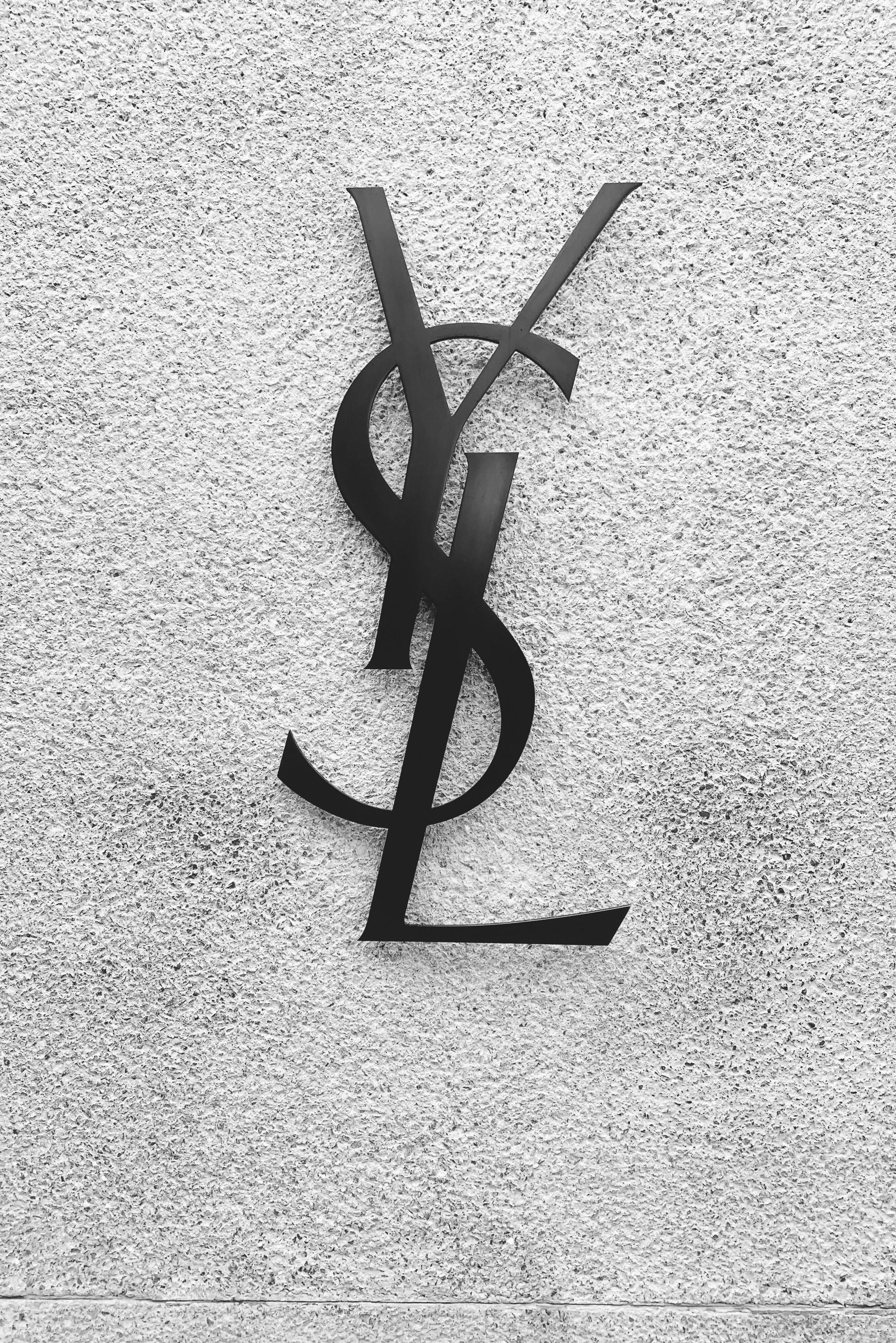 Ysl 桌布 壁紙 — 一個時尚的黑色YSL標誌安裝在粗糙紋理的混凝土牆上，單色調。