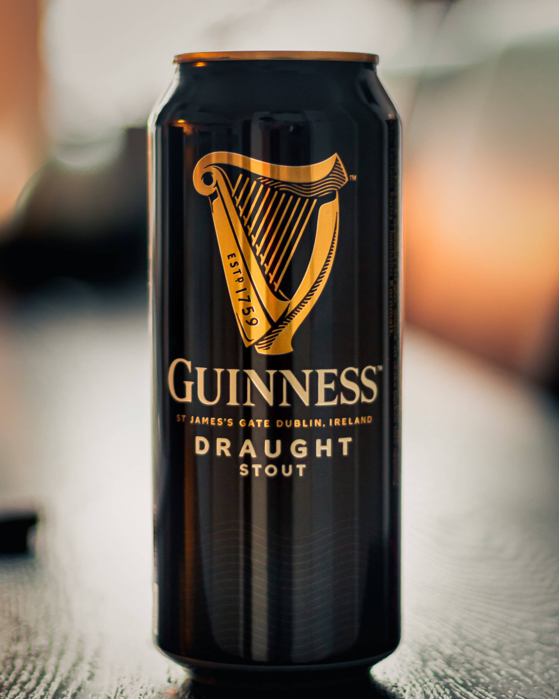 Beer 桌布 壁紙 — 一個時尚的黑色健力士生啤黑啤罐，帶有金色豎琴標誌，在溫暖的環境光下居中放置在帶紋理的表面上。
