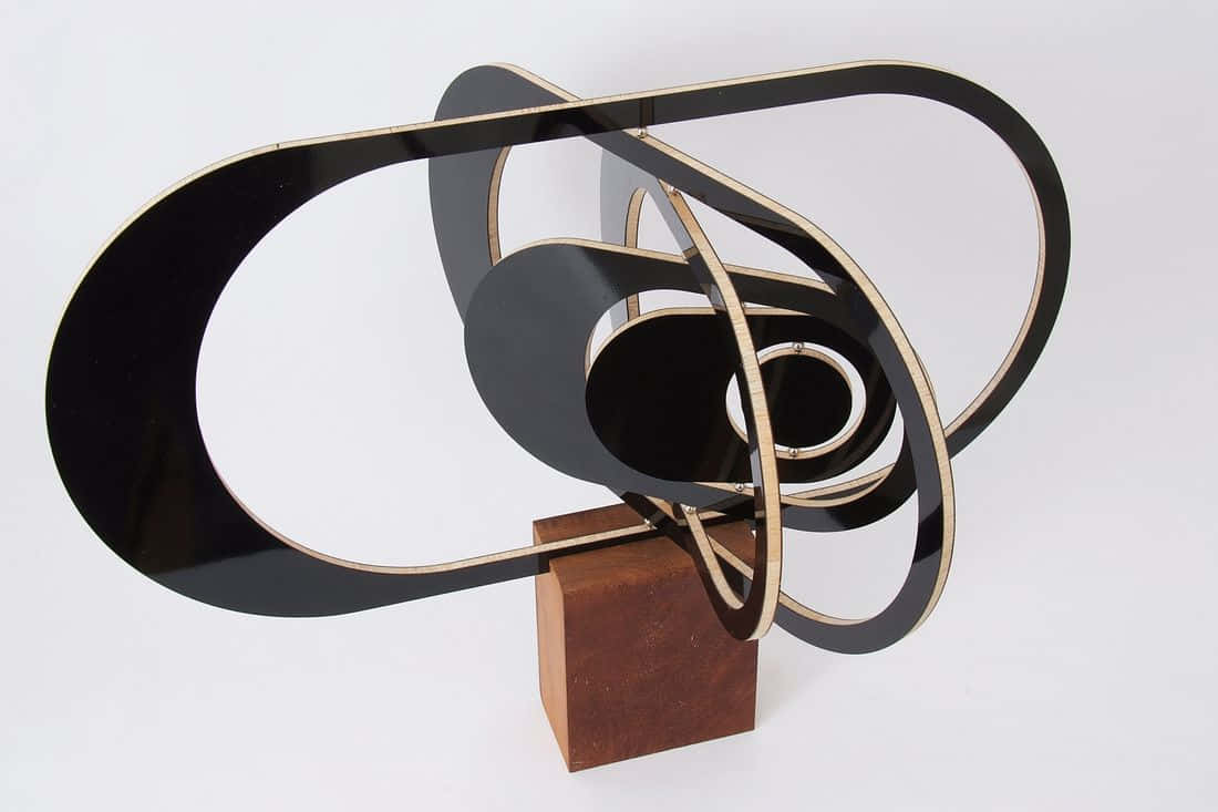 Kinetic Art 桌布 壁紙 — 一個時尚的黑色和金色抽象雕塑，帶有互鎖的環，放置在白色背景的木質底座上。