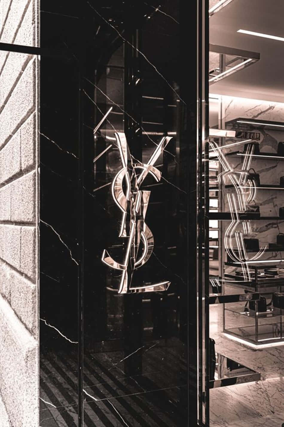 Luxury Aesthetic 桌布 壁紙 — 一個時尚的黑色大理石YSL標誌在豪華精品店的玻璃門上閃耀，配以現代室內照明。
