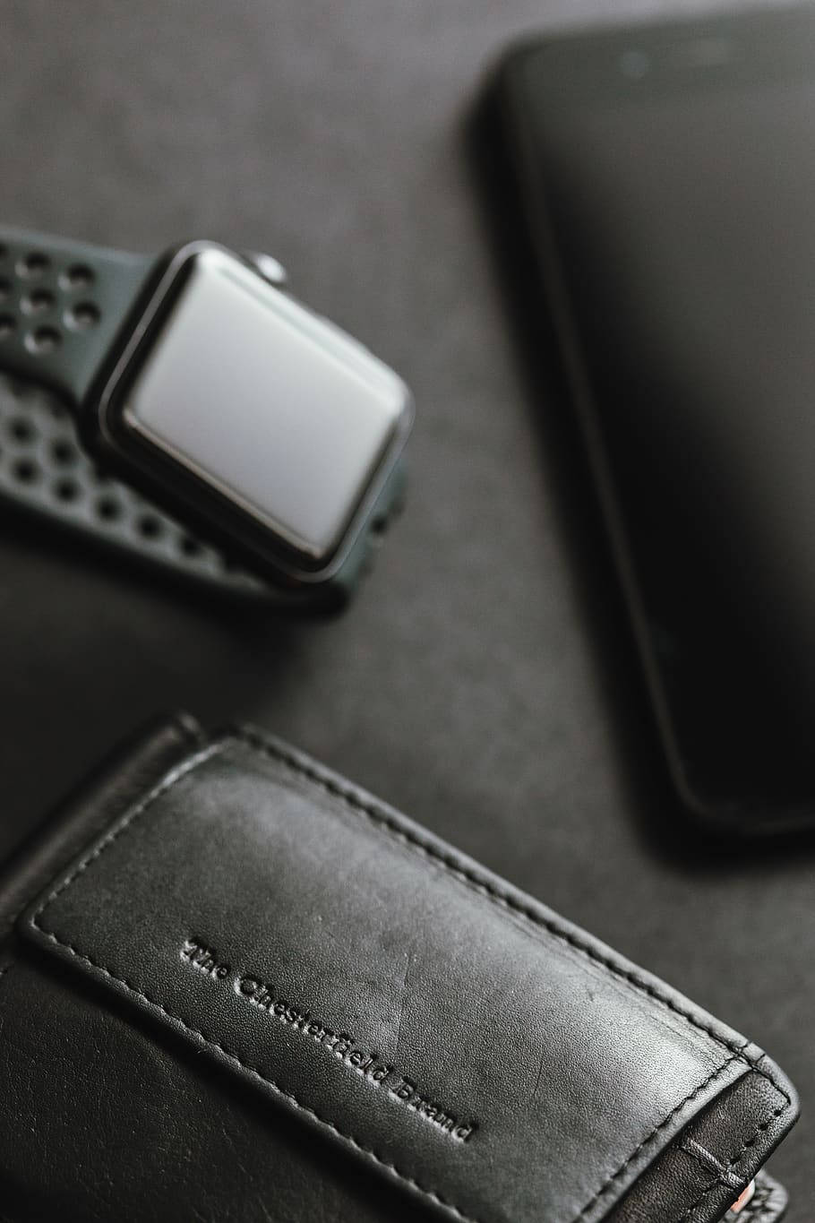 iPhone 桌布 壁紙 — 一個時尚的黑色智慧手錶和手機放在一個深色紋理表面的皮革錢包旁邊。