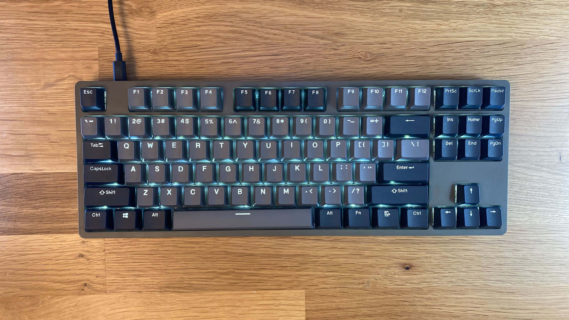 Cute Keyboard 桌布 壁紙 — 一個時尚的黑色機械鍵盤，帶有發光的藍色背光，放置在溫暖的木質桌面上。