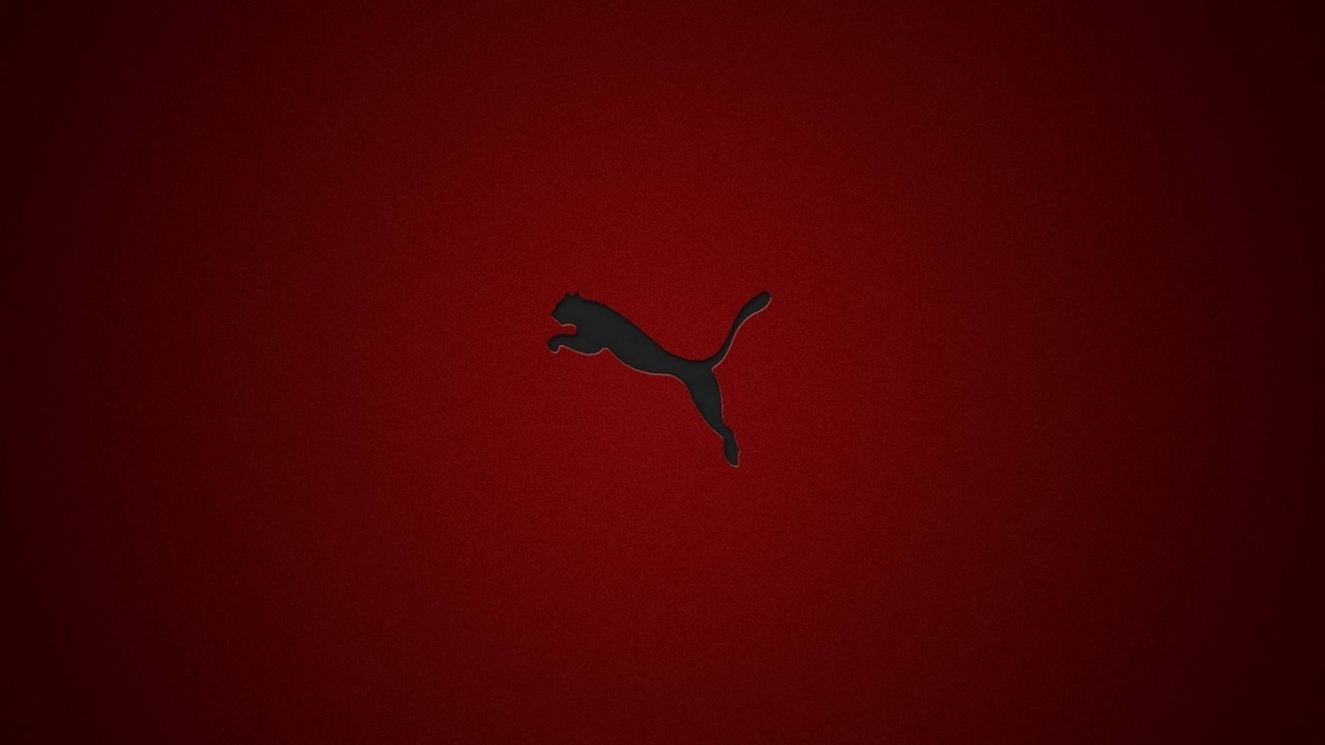 Puma 桌布 壁紙 — 一個時尚的黑色跳躍美洲獅標誌，居中在紋理深紅色背景上。