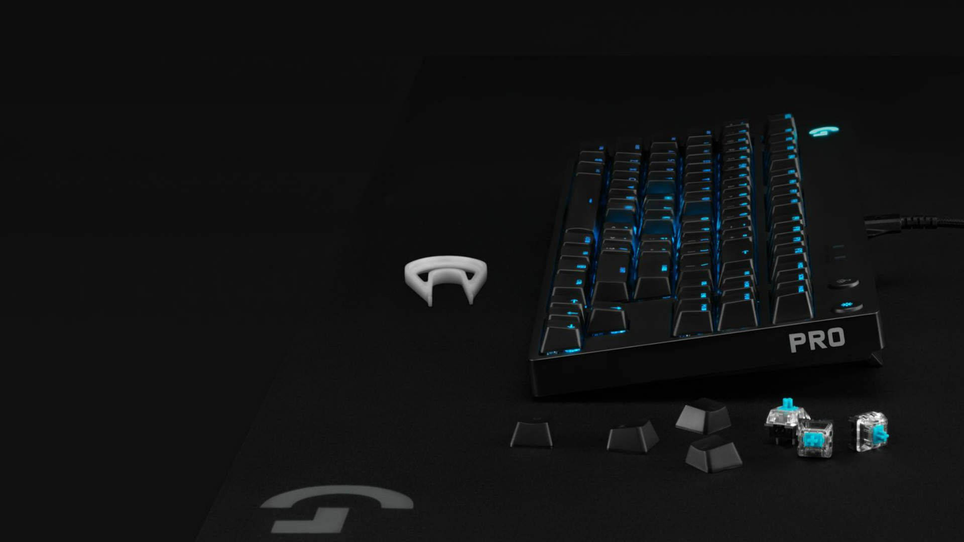 Logitech 桌布 壁紙 — 一個時尚的黑色遊戲鍵盤，帶有藍色背光，放置在深色表面上，周圍是分離的鍵帽和機械開關。