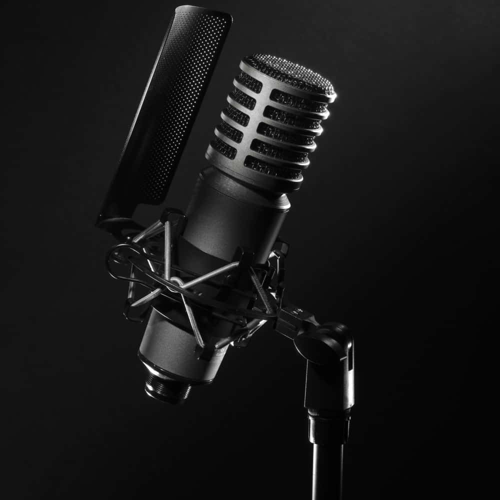 Sound 桌布 壁紙 — 一個時尚的黑色錄音室麥克風，配有防噴罩和防震架，孤立地立在深色背景前。