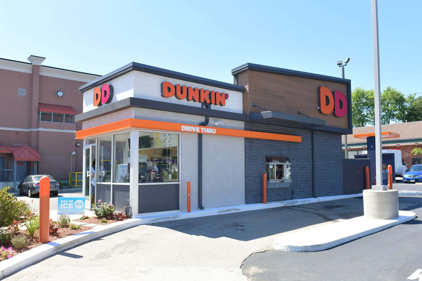 Dunkin Donuts 桌布 壁紙 — 一個晴朗的日子，在現代化的Dunkin'得來速，帶有橙色點綴和清澈的藍天。