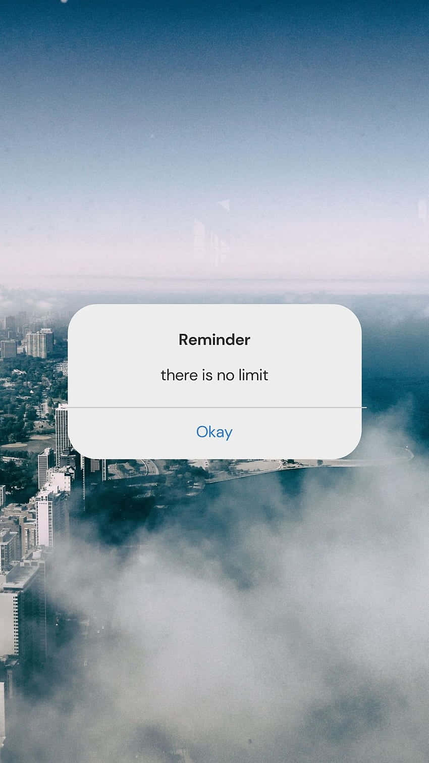 Aesthetic Reminder 桌布 壁紙 — 一個智慧型手機通知，上面寫著「Reminder there is no limit」，漂浮在從上方看到的霧氣瀰漫的城市景觀之上。