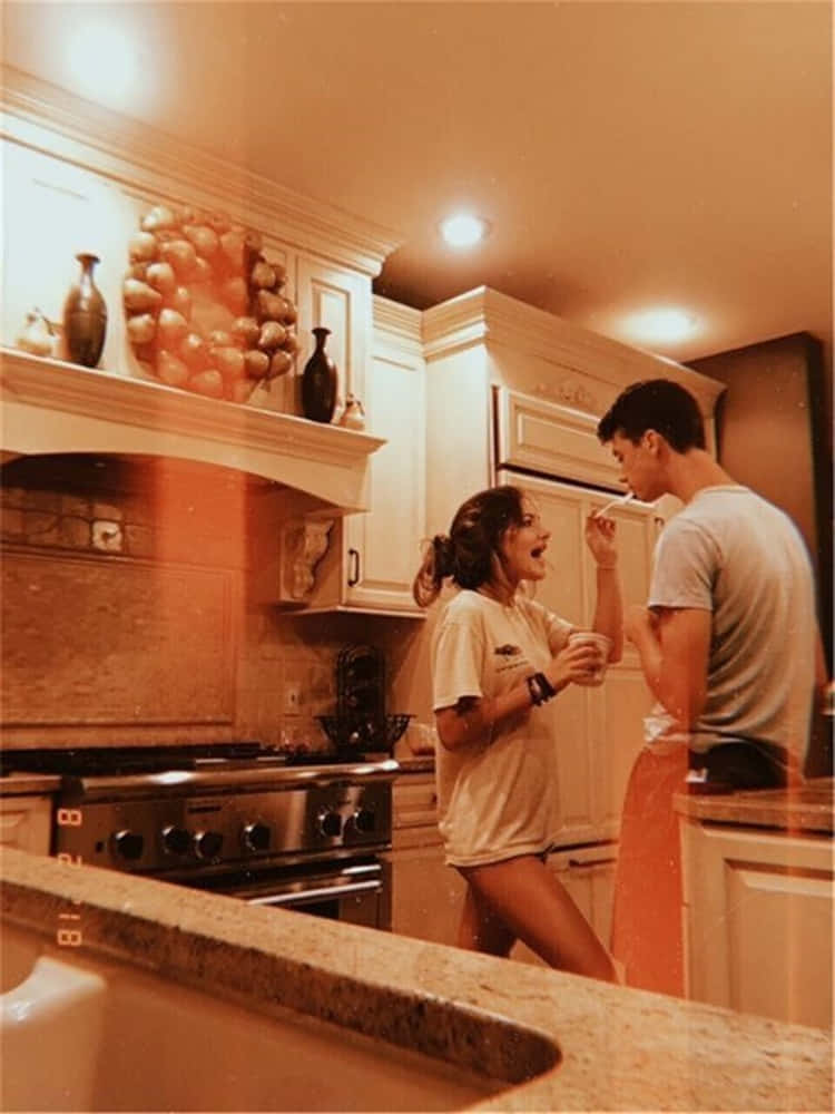 Girlfriend And Boyfriend 桌布 壁紙 — 一個暖色調的廚房場景，兩個人在櫃檯附近笑著分享一個俏皮的時刻。