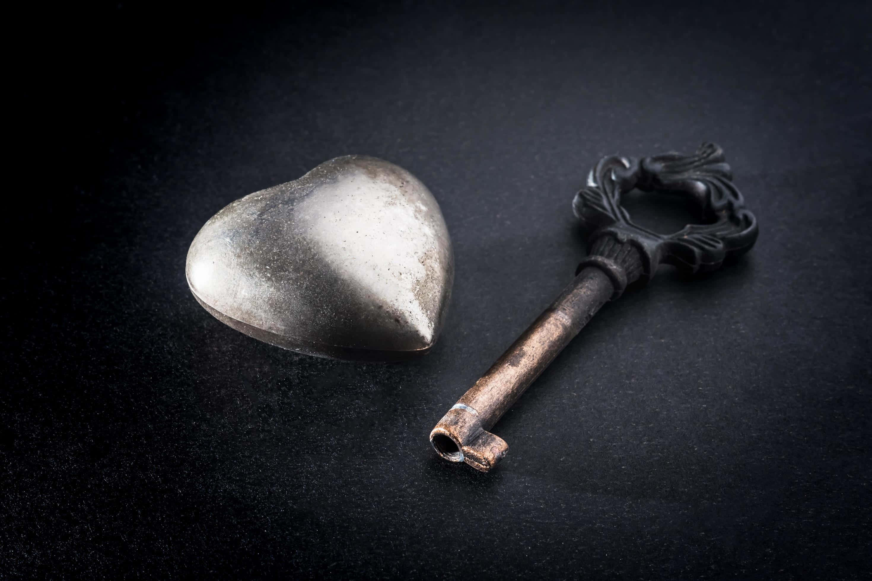Dark Love 桌布 壁紙 — 一個暗淡的心形金屬物體和一個華麗的復古鑰匙，在戲劇性的燈光下，放置在深色紋理表面上。
