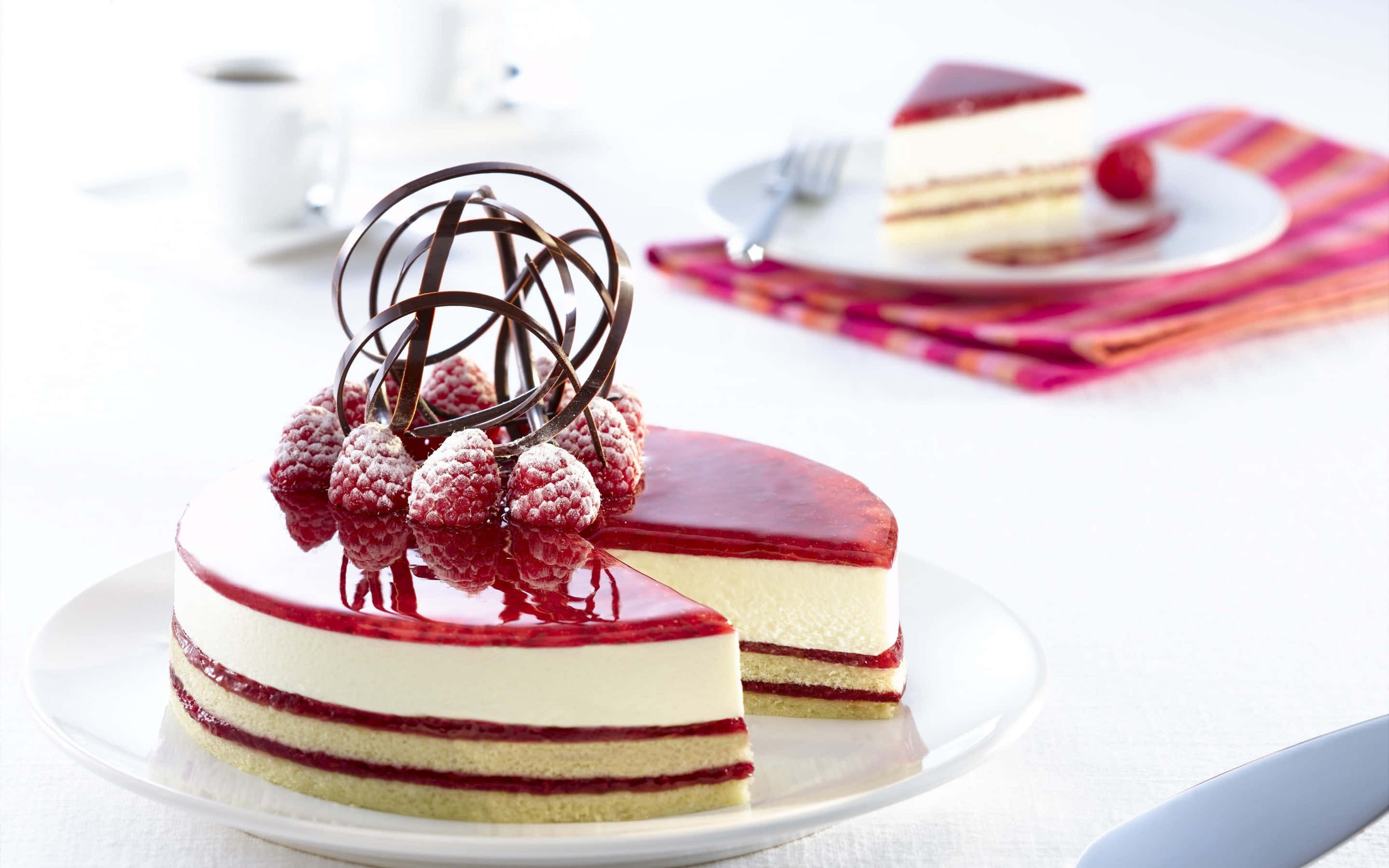 Desserts 桌布 壁紙 — 一個有光澤的紅桑子起司蛋糕，帶有巧克力漩渦和新鮮莓果，放在白色盤子上，旁邊有一片蛋糕。