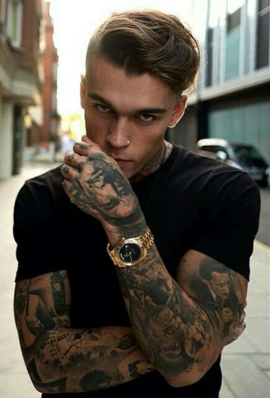 Tattoo Boy 桌布 壁紙 — 一個有刺青、戴鼻環和金錶的男人，在城市街道上將刺青的手放在臉附近，眼神專注。