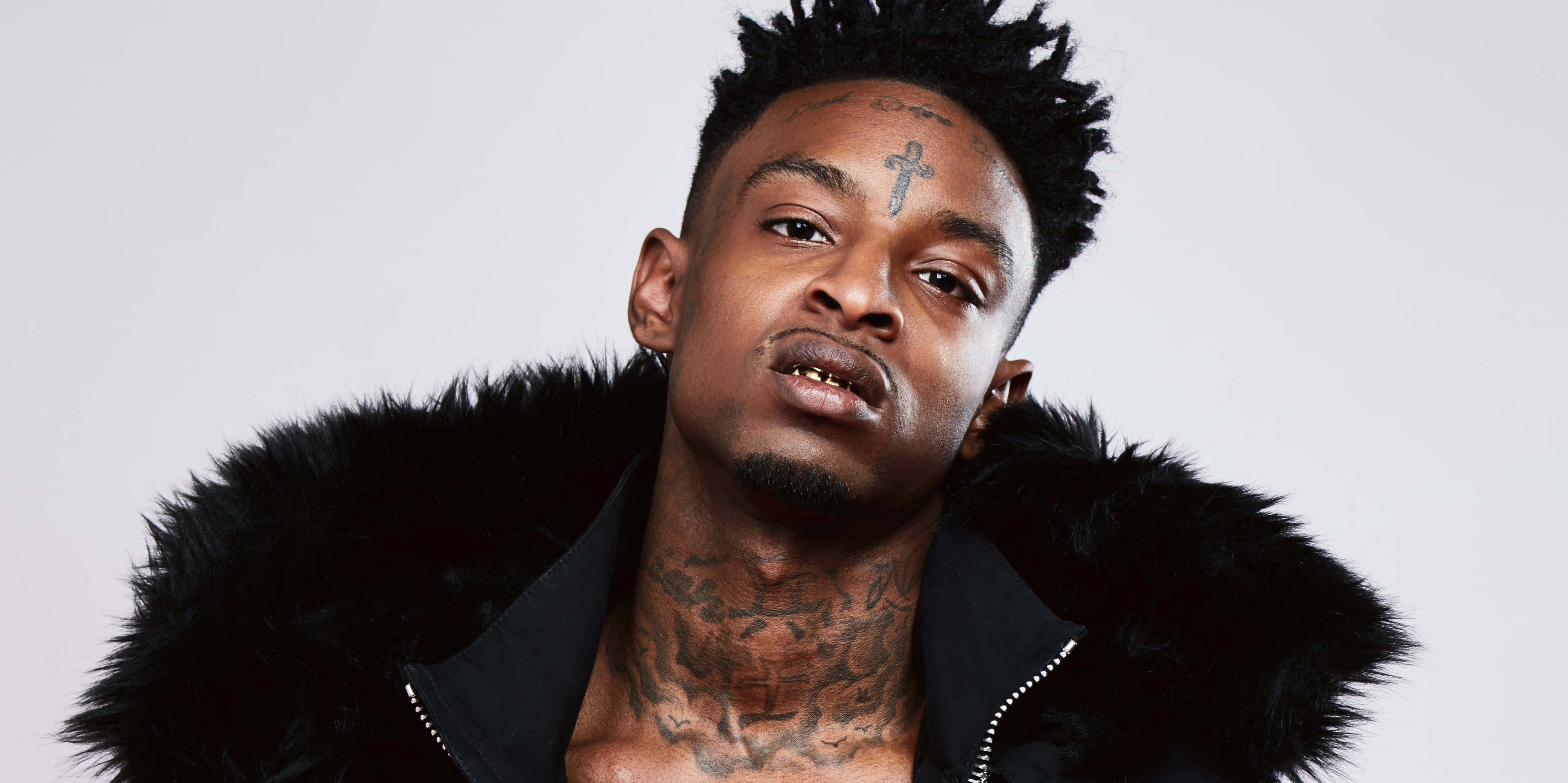 21 Savage 桌布 壁紙 — 一個有刺青、穿著黑色毛領外套的男人，在純白色背景下強烈地凝視。