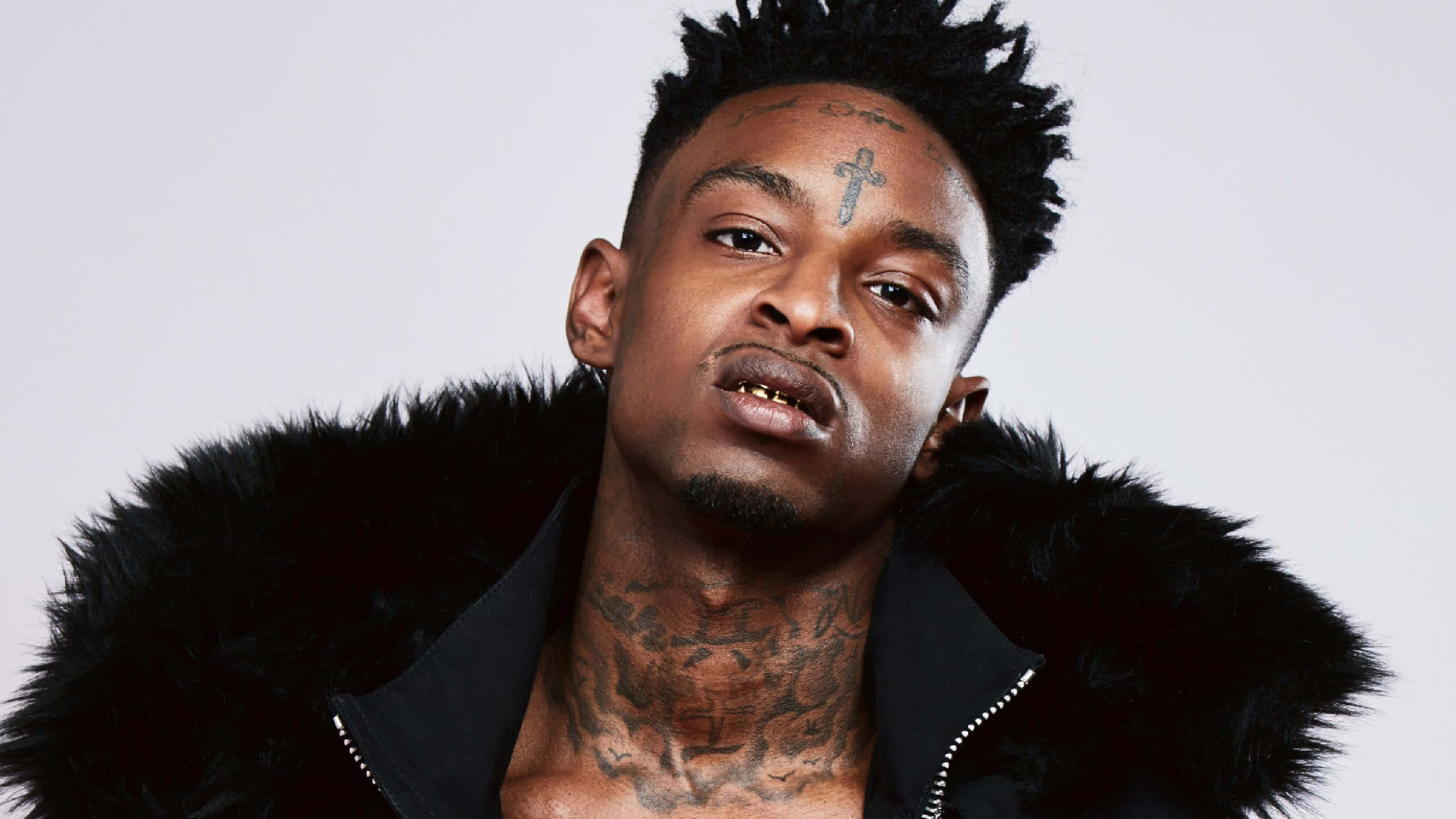 21 Savage 桌布 壁紙 — 一個有刺青、身穿黑色毛領外套的男人，在純白背景下強烈凝視。