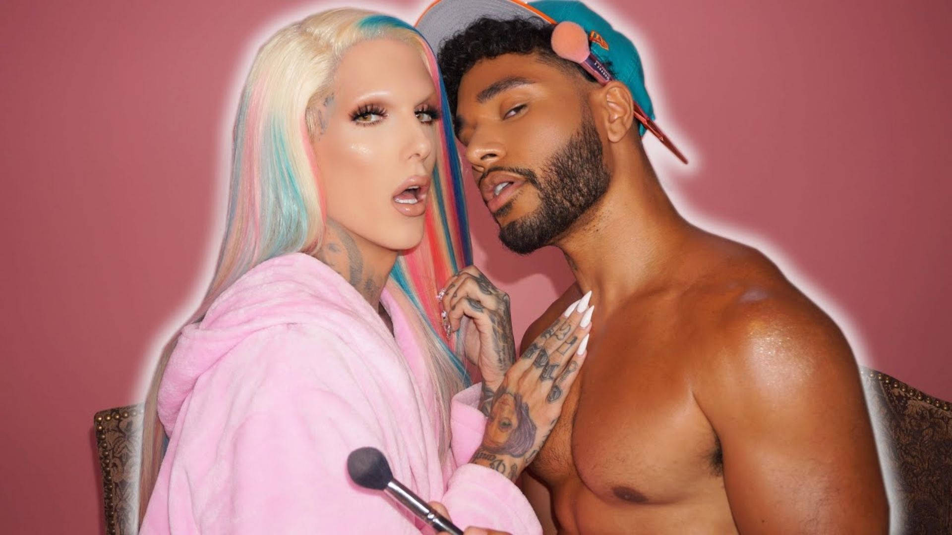 Jeffree Star 桌布 壁紙 — 一個有刺青和彩色頭髮的男人和女人在粉紅色的牆前親密地擺姿勢，拿著化妝刷。