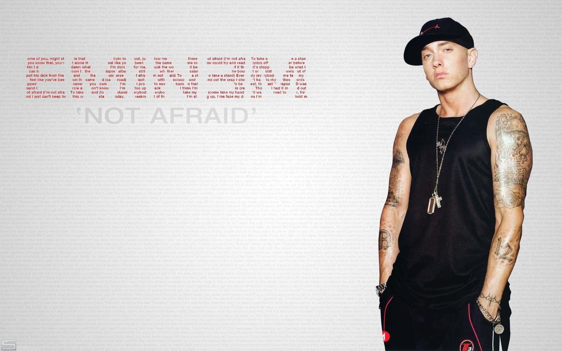 阿姆 桌布 壁紙 — 一個有刺青和戴帽子的男人自信地站在他歌曲《Not Afraid》的歌詞旁邊，背景是純色的。