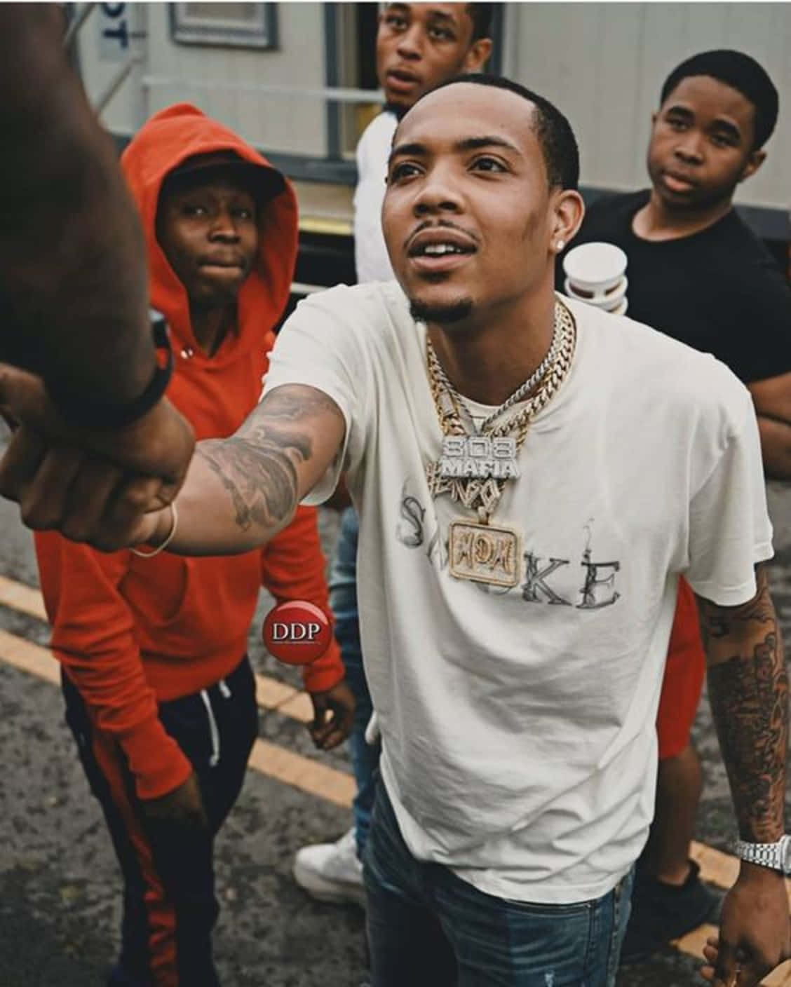 Herbo iPhone 桌布 壁紙 — 一個有刺青和戴金項鍊的年輕男子在破舊的城市街道上與朋友自拍。