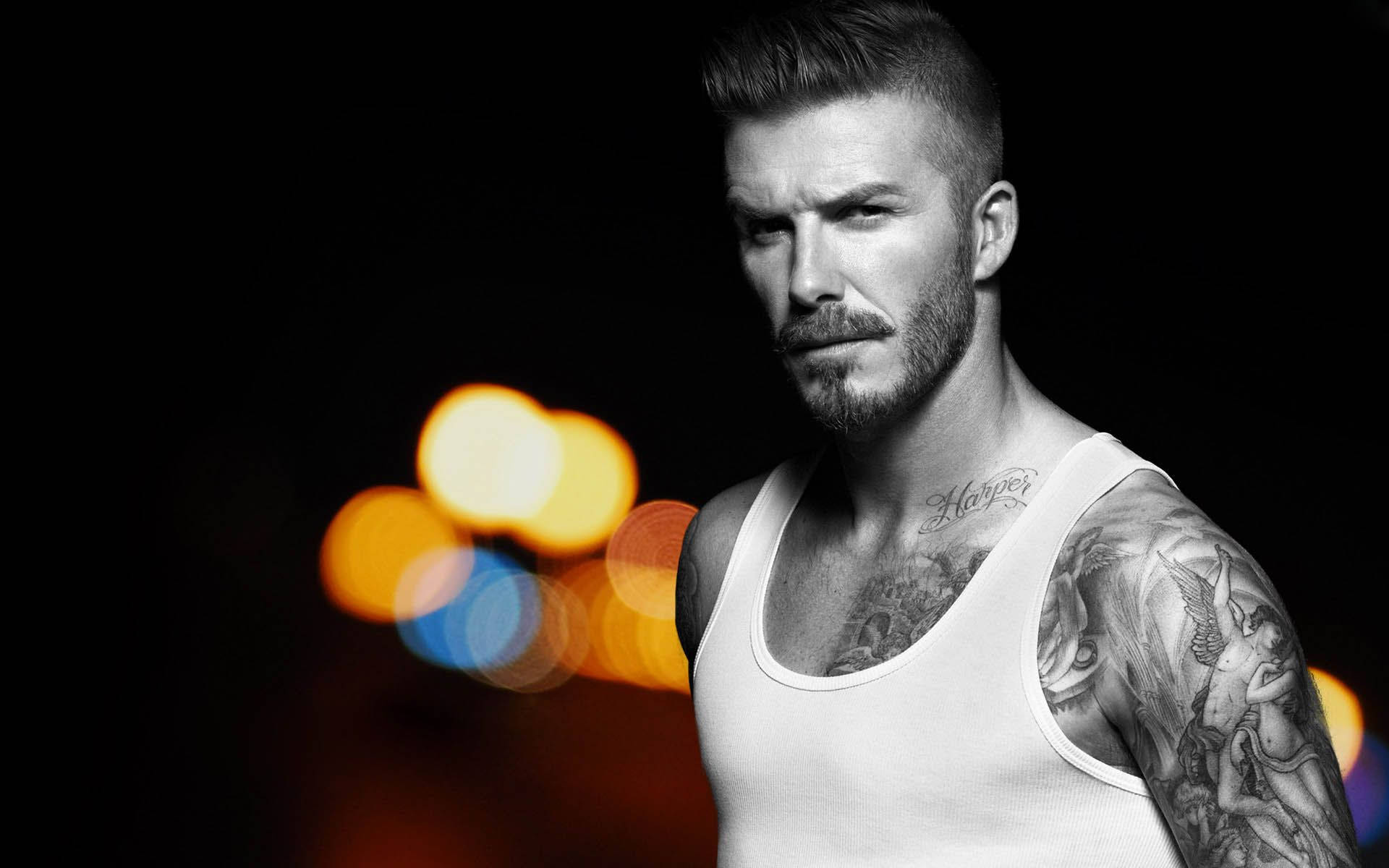 David Beckham 桌布 壁紙 — 一個有刺青和鬍鬚的男人在黑暗背景中專注地凝視，背景有彩色散景燈光。