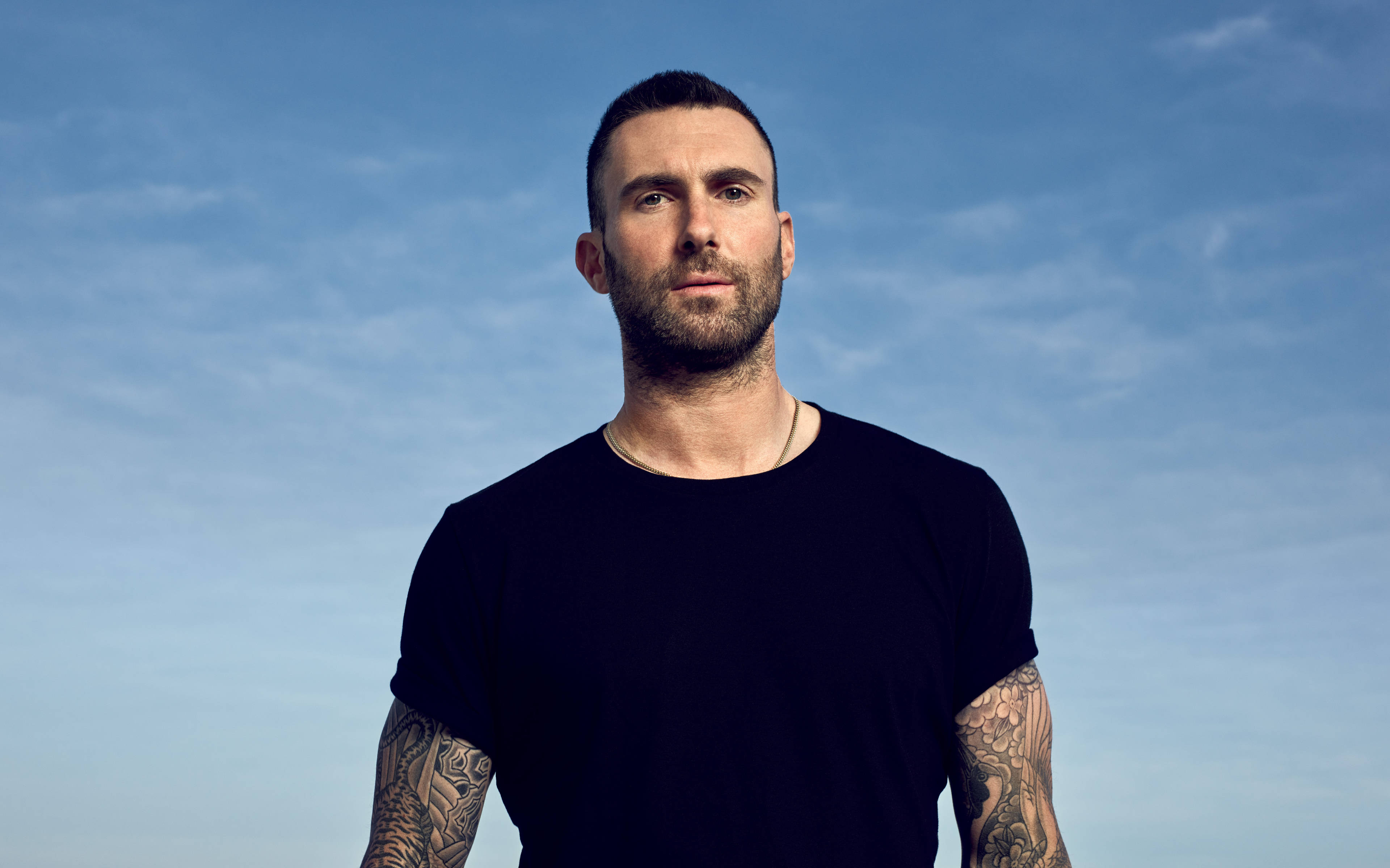 Adam Levine 桌布 壁紙 — 一個有刺青和鬍鬚的男人站在清澈的藍天下，穿著黑色T恤。