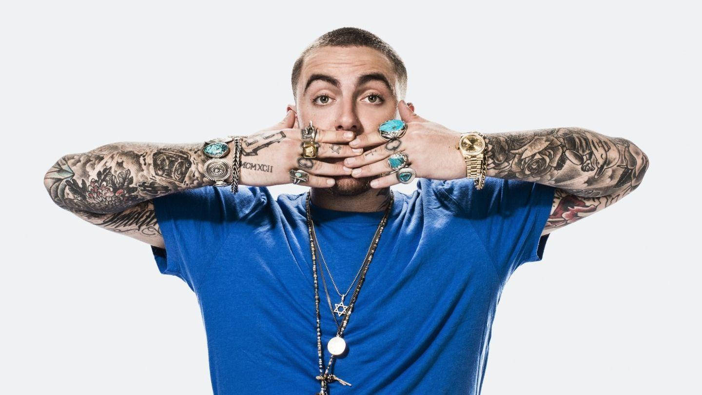 Mac Miller 桌布 壁紙 — 一個有刺青手臂和戴著多個戒指的男人，在純白色背景前用雙手捂住嘴巴。