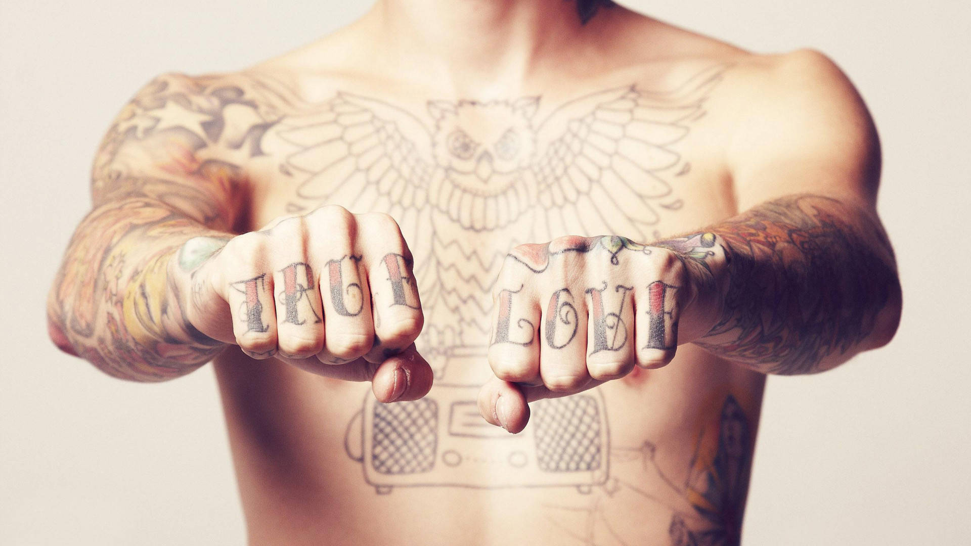 Tattoo 桌布 壁紙 — 一個有刺青的人展示拳頭，拳頭指節上刺有「TRUE LOVE」，背景為純色。