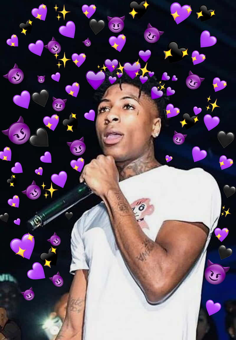 Youngboy Never Broke Again 桌布 壁紙 — 一個有刺青的年輕男子拿著麥克風，紫色愛心和惡魔表情符號在黑暗背景中漂浮在他周圍。