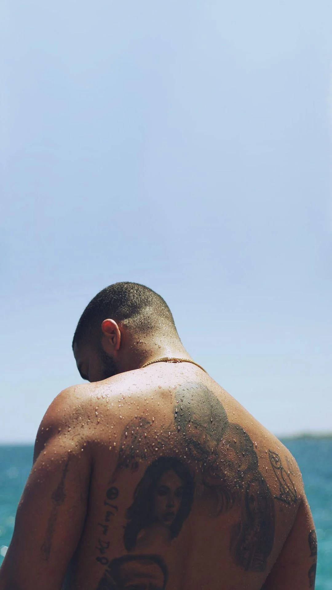 Drake 桌布 壁紙 — 一個有刺青的男人，皮膚濕潤，赤膊站在海邊，在清澈的藍天下。