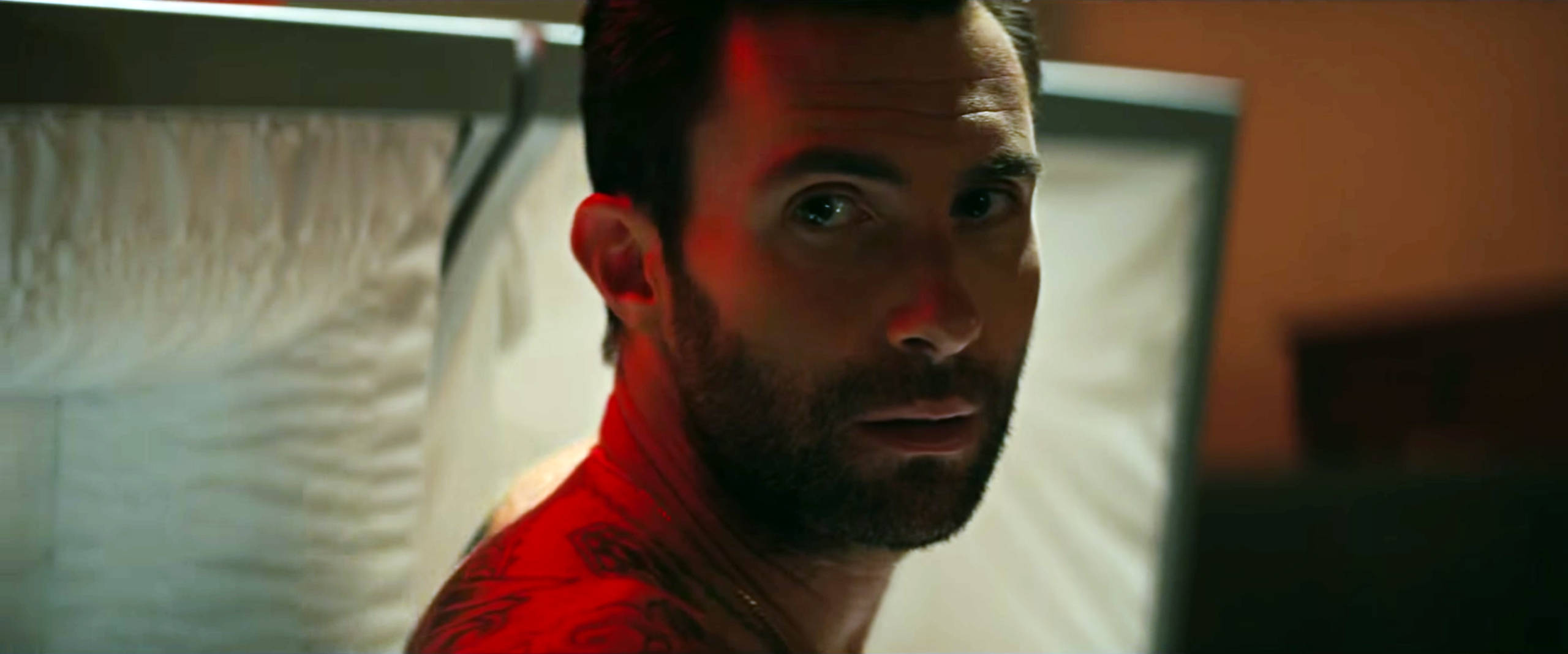 Adam Levine 桌布 壁紙 — 一個有刺青的男人在昏暗的房間裡，白色窗簾下，紅色燈光中專注地凝視。