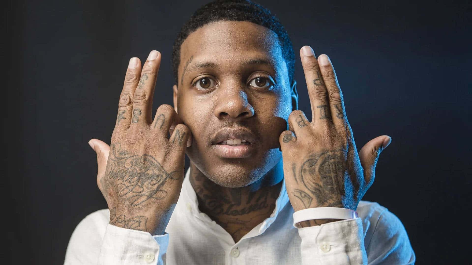 Lil Durk 桌布 壁紙 — 一個有刺青的男人在黑暗背景前，在冷藍色燈光下用手框住自己的臉。