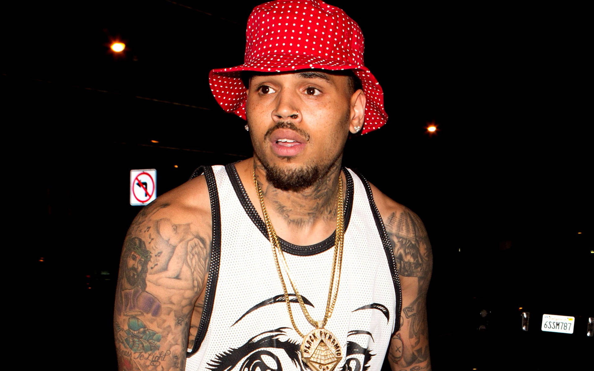 Chris Brown 桌布 壁紙 — 一個有刺青的男人戴著紅色圓點帽子和金鏈，背景是漆黑的夜晚。