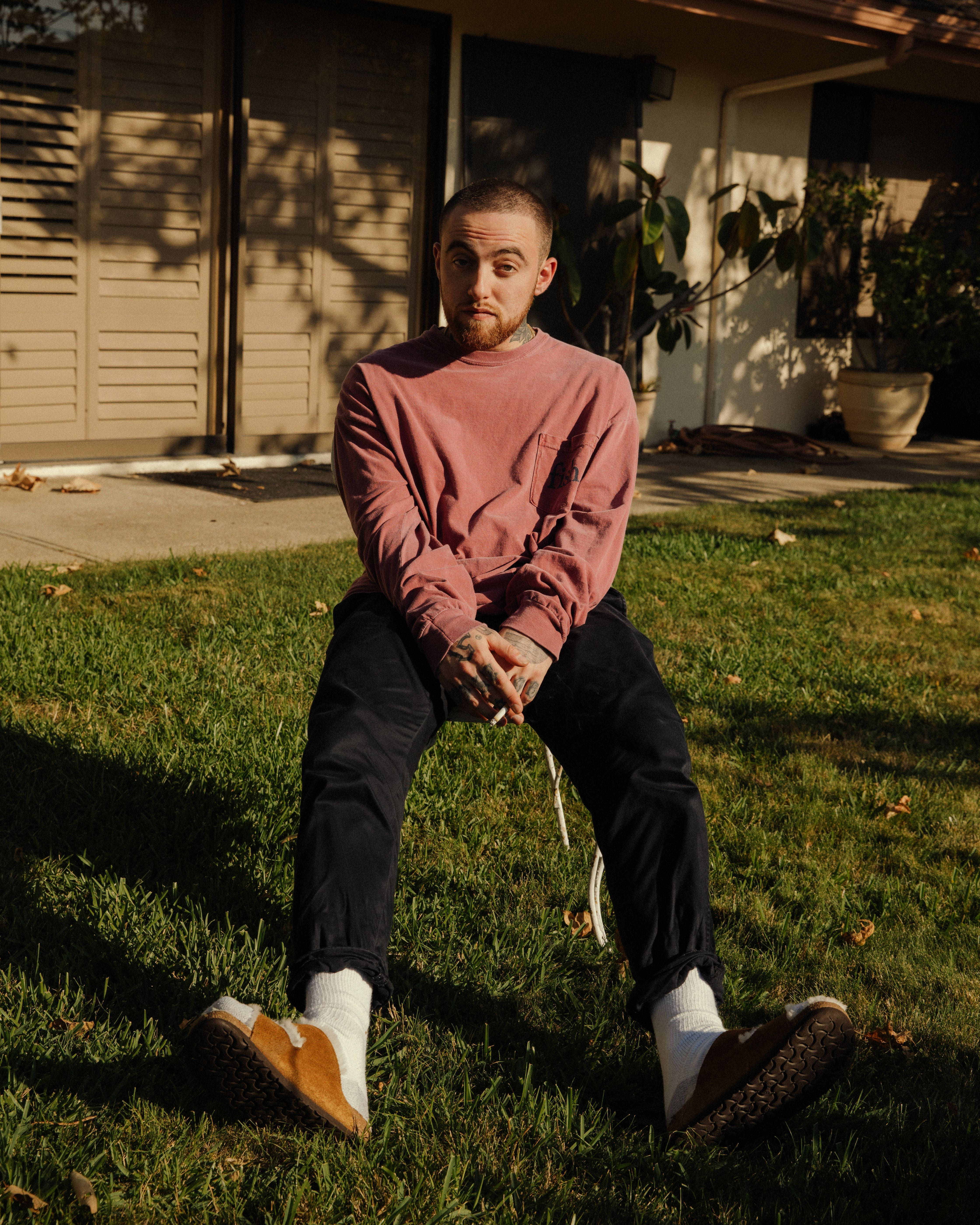 mac miller 4K 桌布 壁紙 — 一個有刺青的男人盤腿坐在屋前的草地上，屋外沐浴在溫暖的金色陽光中。