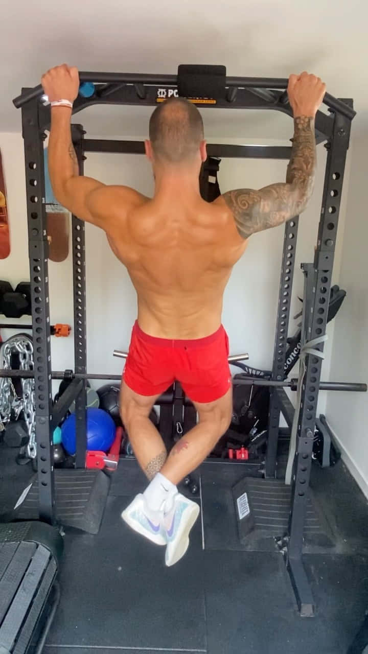 Fitness 桌布 壁紙 — 一個有刺青的肌肉男在家庭健身房的引體向上桿上做引體向上，穿著紅色短褲和白色運動鞋。