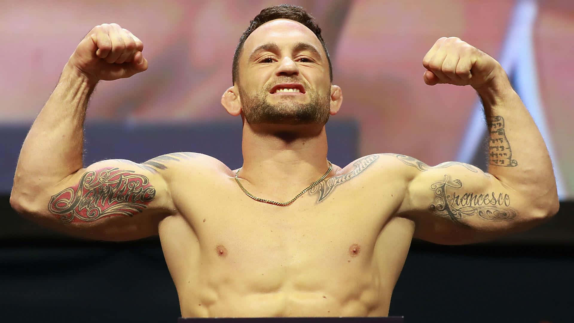 UFC 桌布 壁紙 — 一個有刺青的肌肉男在明亮的舞台燈光下以勝利姿勢彎曲雙臂。